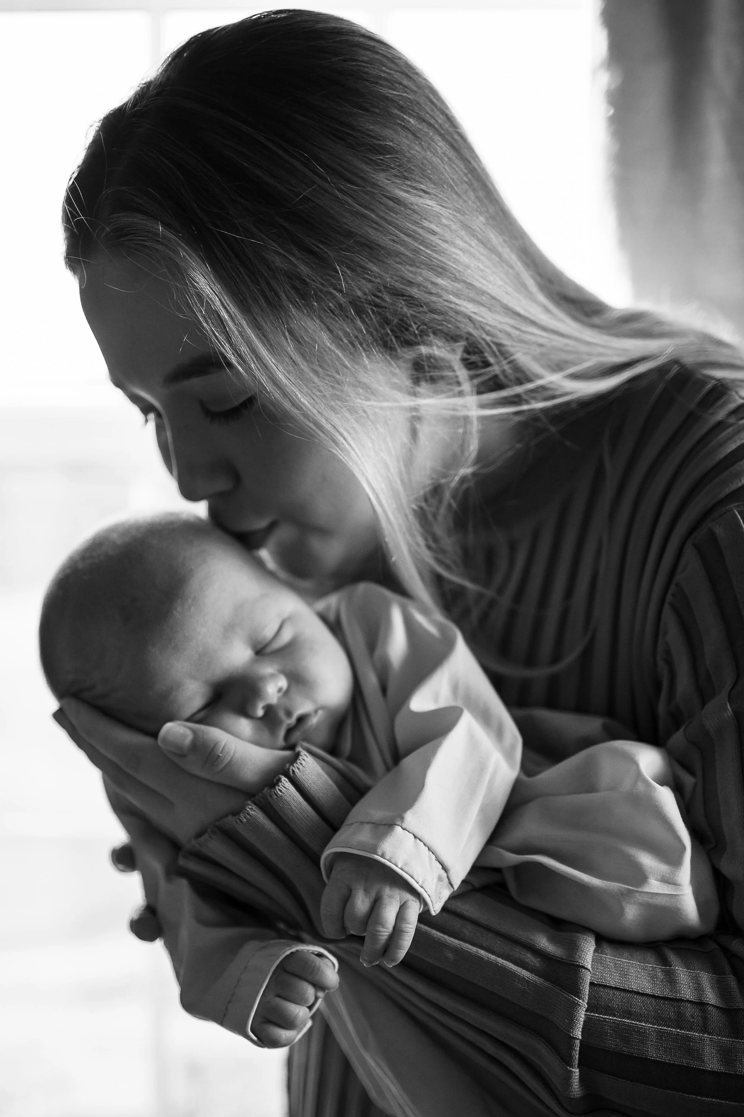 A woman gently holding a sleeping baby close, with her head bowed and touching the baby's head in a tender and comforting pose.