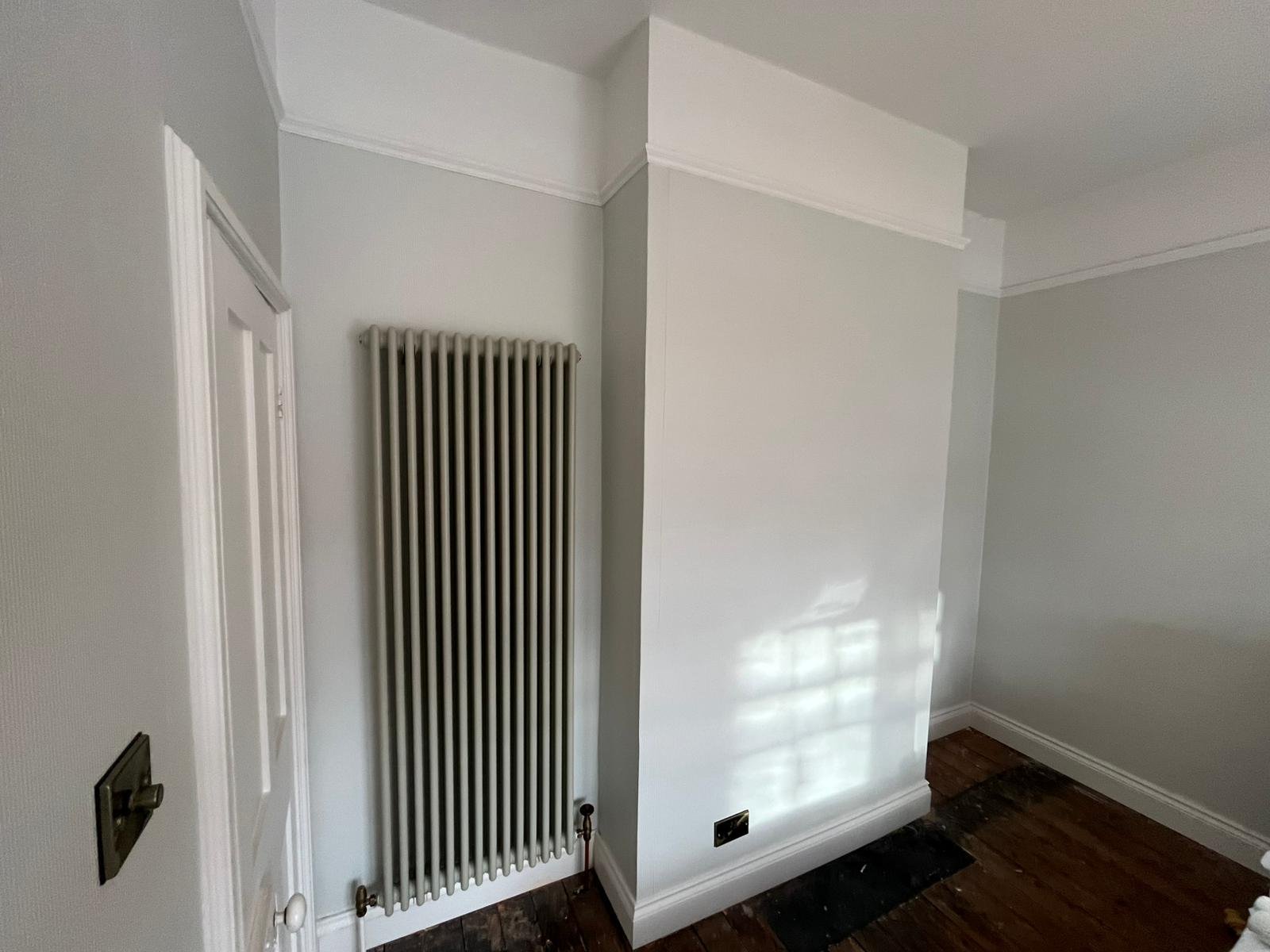 Empty room with white walls, a radiator, a door with a silver handle, and wooden flooring.