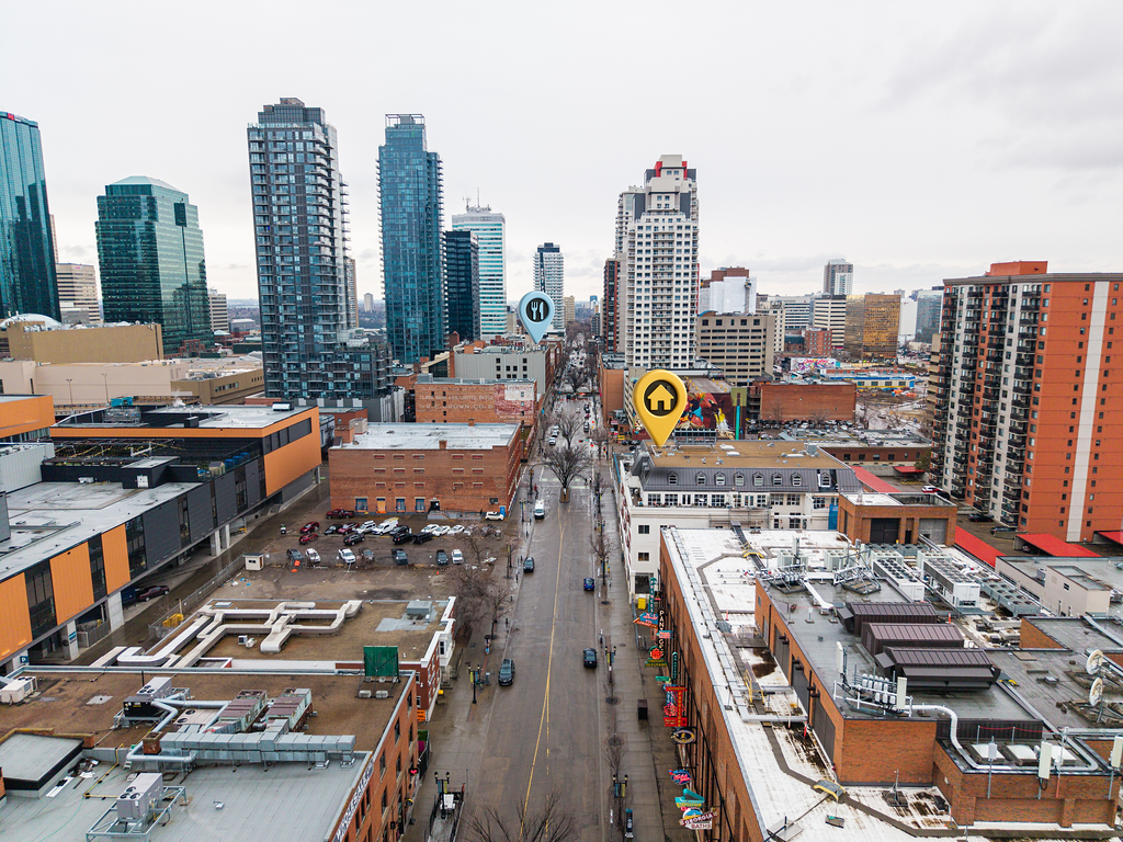 Downtown cityscape with tall skyscrapers and mid-rise buildings, streets with parked cars, and outdoor signage.