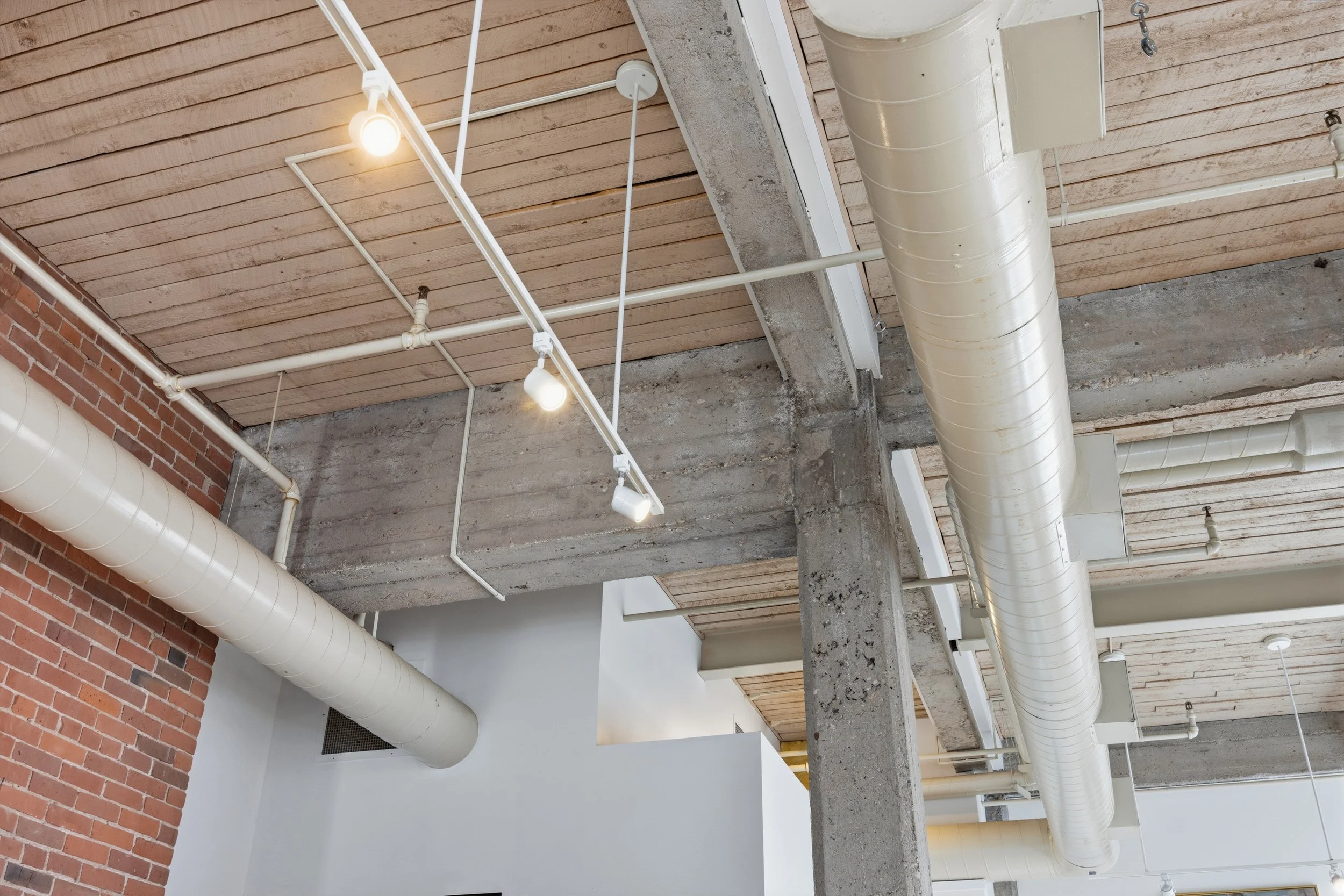 Ceiling with exposed industrial piping, ductwork, and wooden ceiling panels in a modern interior space.