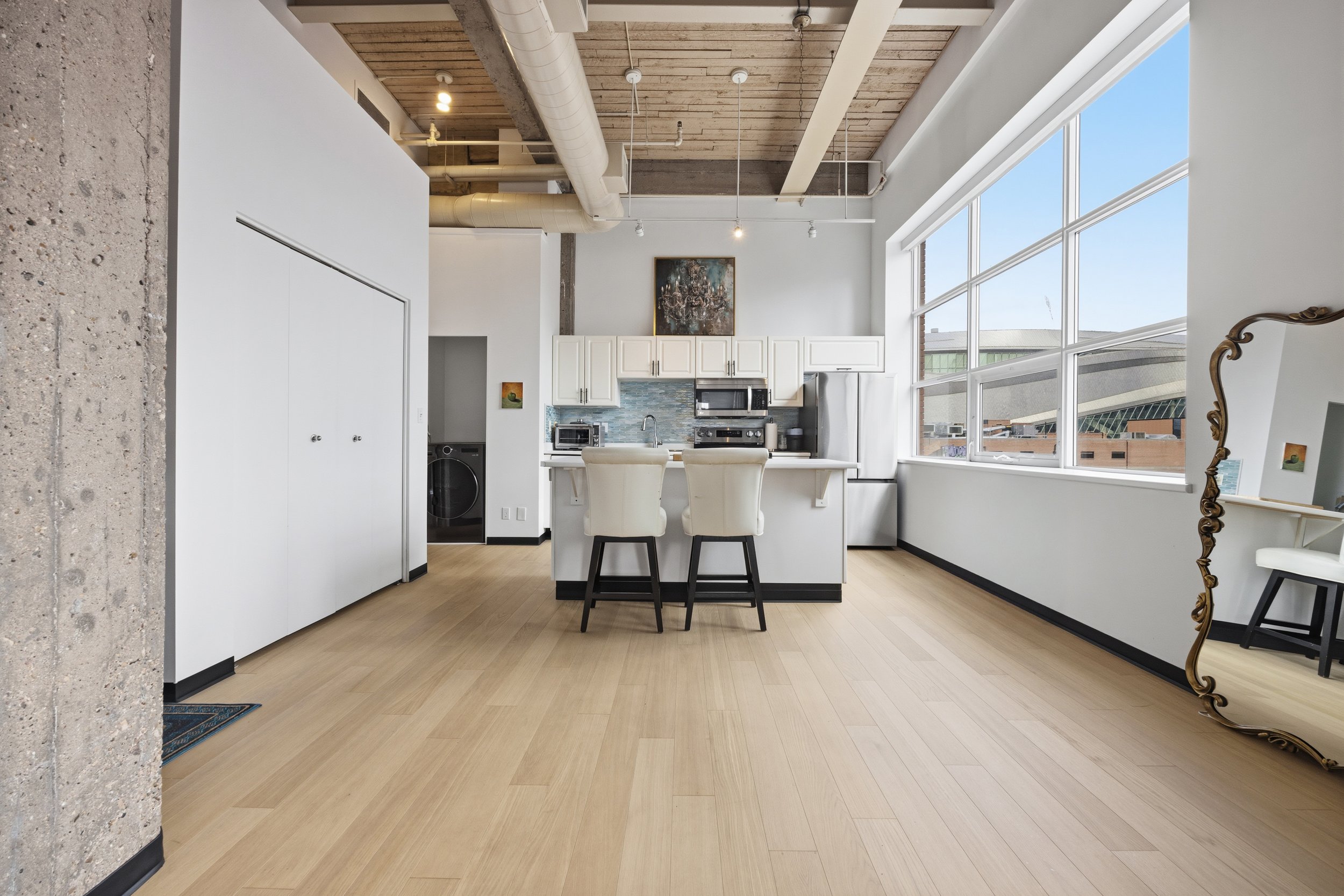 Modern kitchen with large windows, white cabinets, kitchen appliances, and a breakfast bar with two chairs.