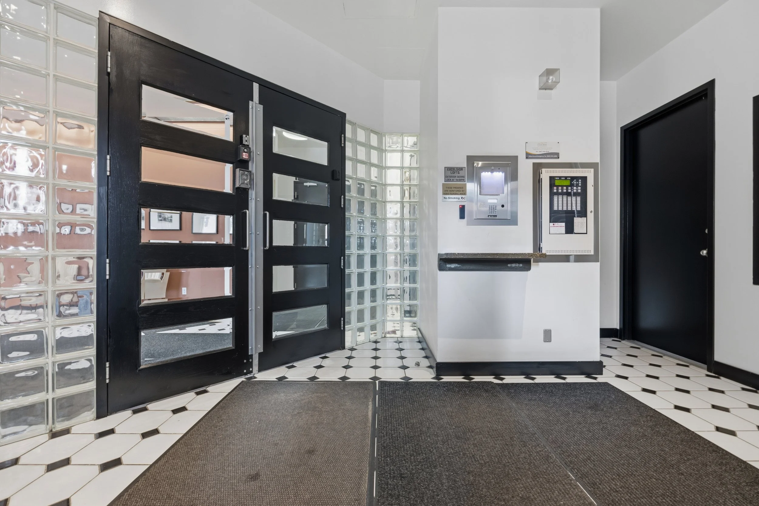 Interior view of an entrance with black double doors, glass brick walls, and black and white tiled flooring.