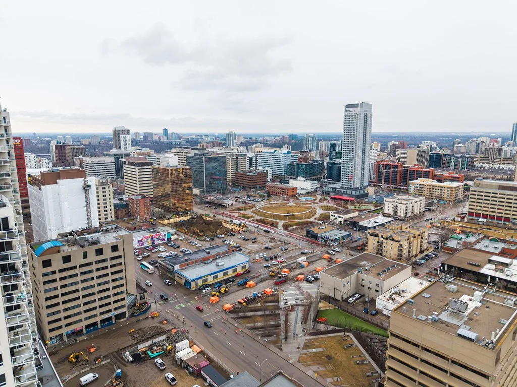 A cityscape view from a high-rise building showing numerous buildings, roads, and parking lots under an overcast sky.