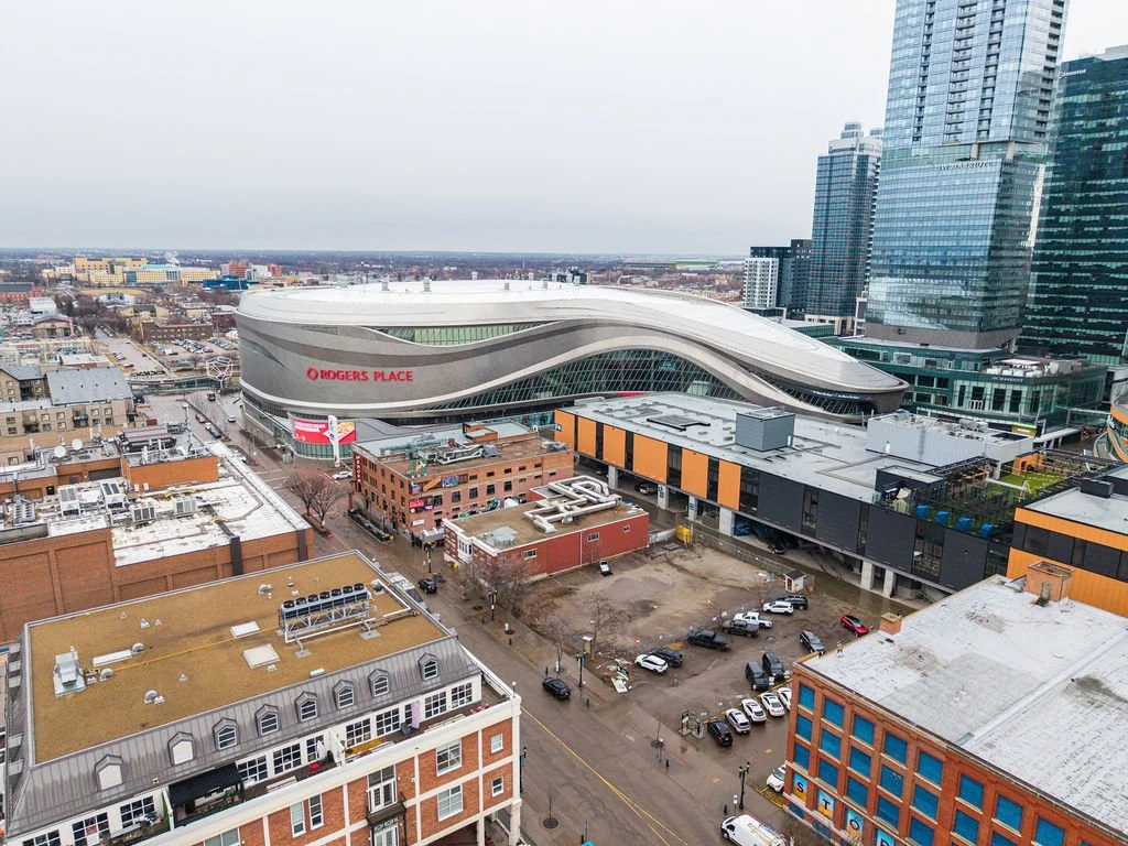 A cityscape with Rogers Place sports arena, modern high-rise buildings, and older brick buildings on a cloudy day.