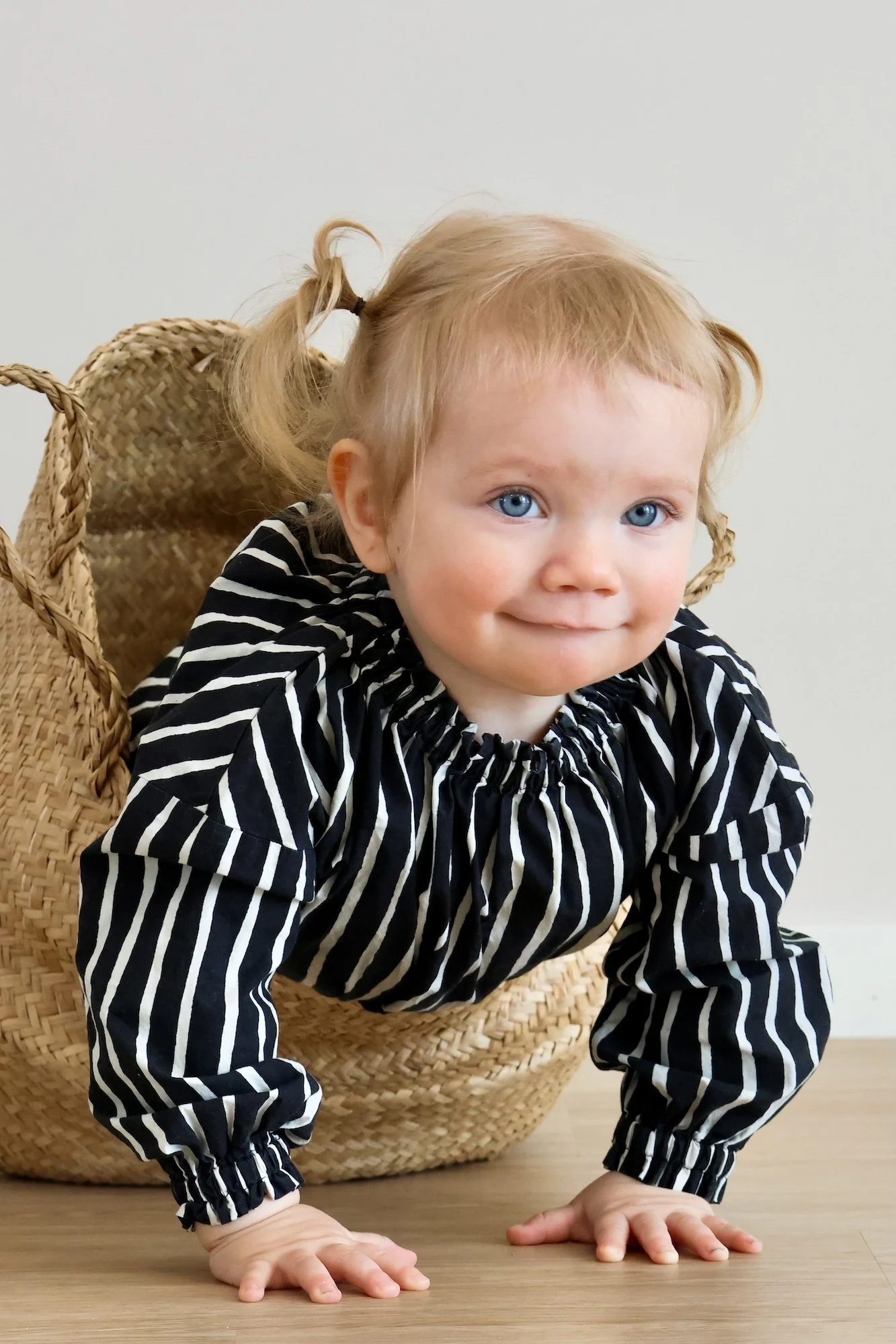 Pieni tyttö perhekuvauksessa lattialla, pukeutuneena mustavalkoraidalliseen puseroon.