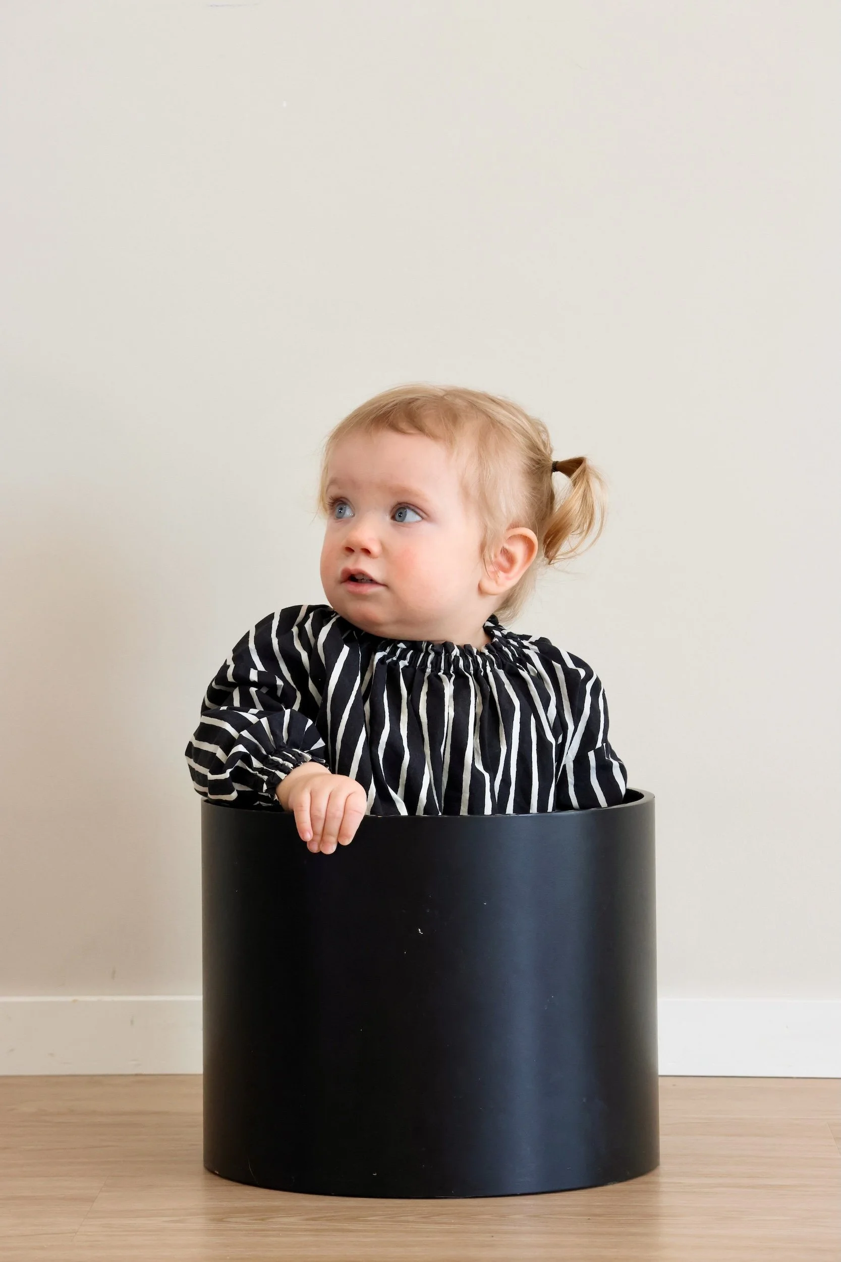 Pikku tyttö istuu perhekuvauslokaatiossa ja katsoo vasemmalle puolelle.