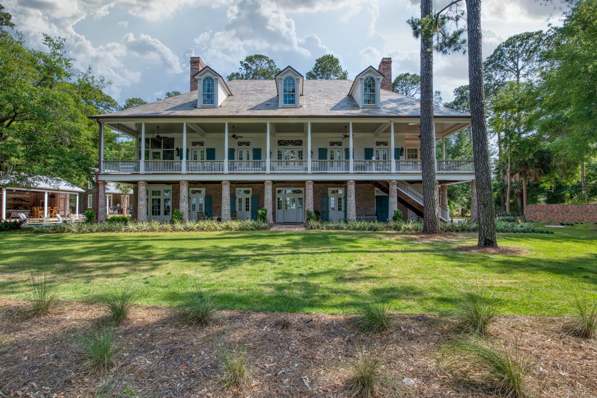 Large two-story house with a wraparound porch, surrounded by trees and a lawn.