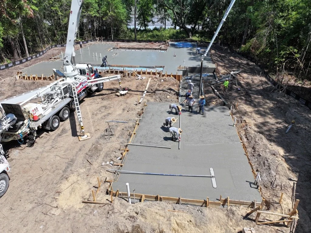 Construction workers pouring concrete for building foundations at a construction site surrounded by trees.