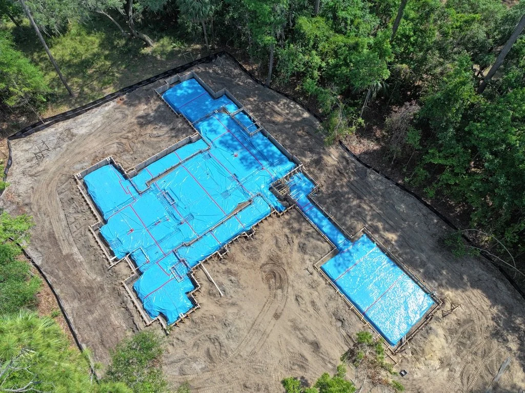 Aerial view of a house under construction, covered with blue tarps, surrounded by trees.