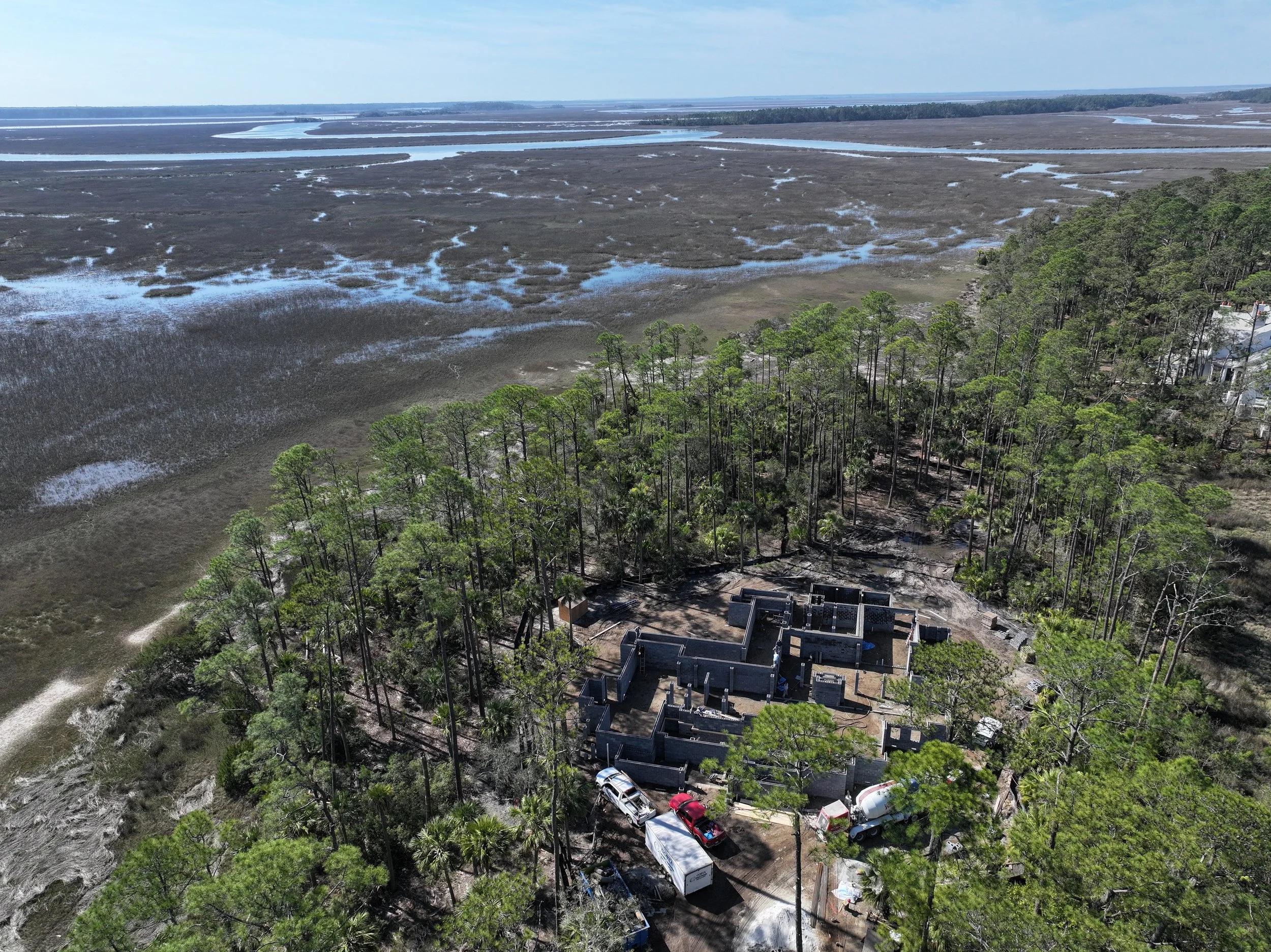 Aerial view of a large, historic stone building surrounded by forests, with wetlands and water bodies in the distance.