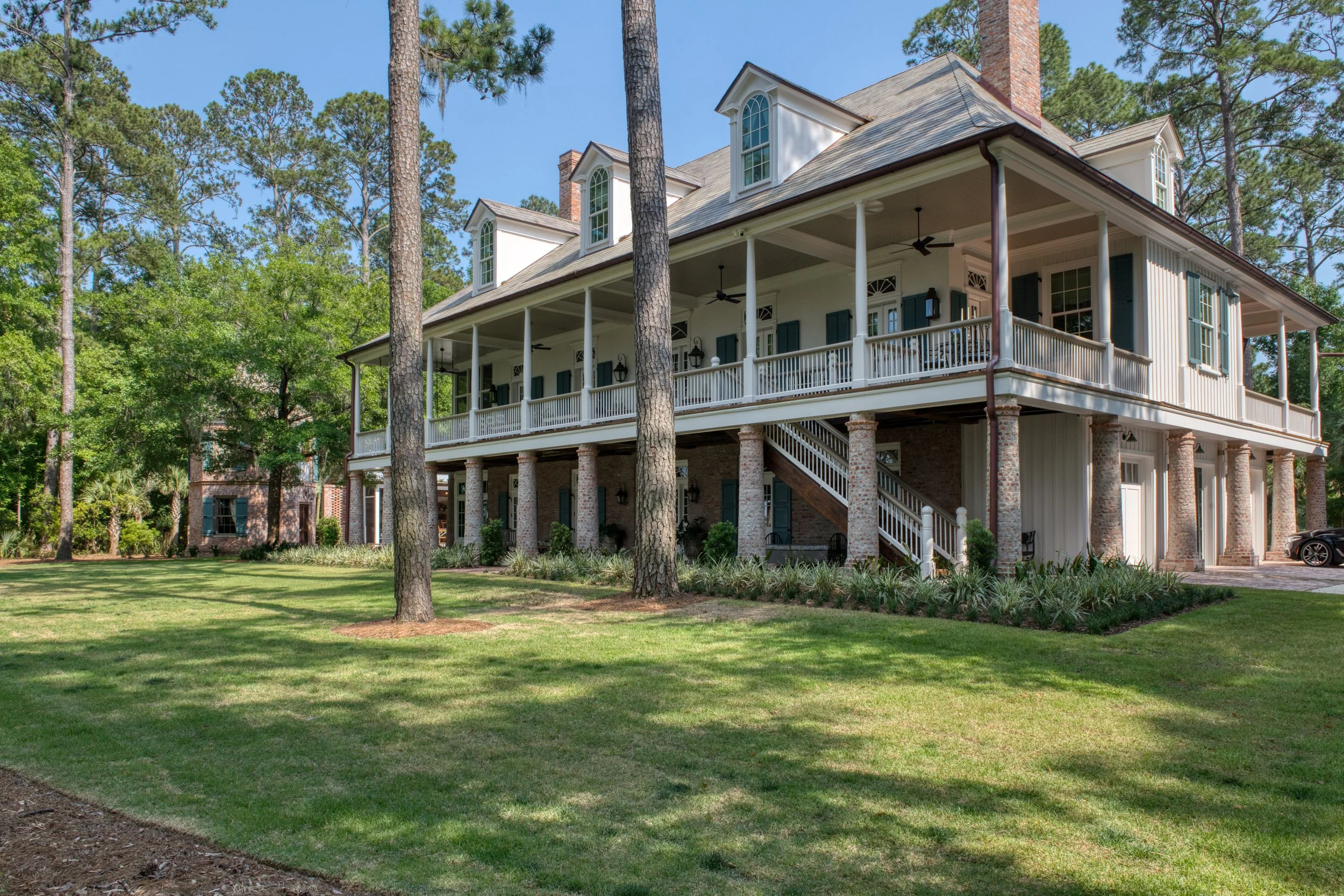Large two-story house with a wrap-around porch, brick and wood exterior, surrounded by grass and tall trees.