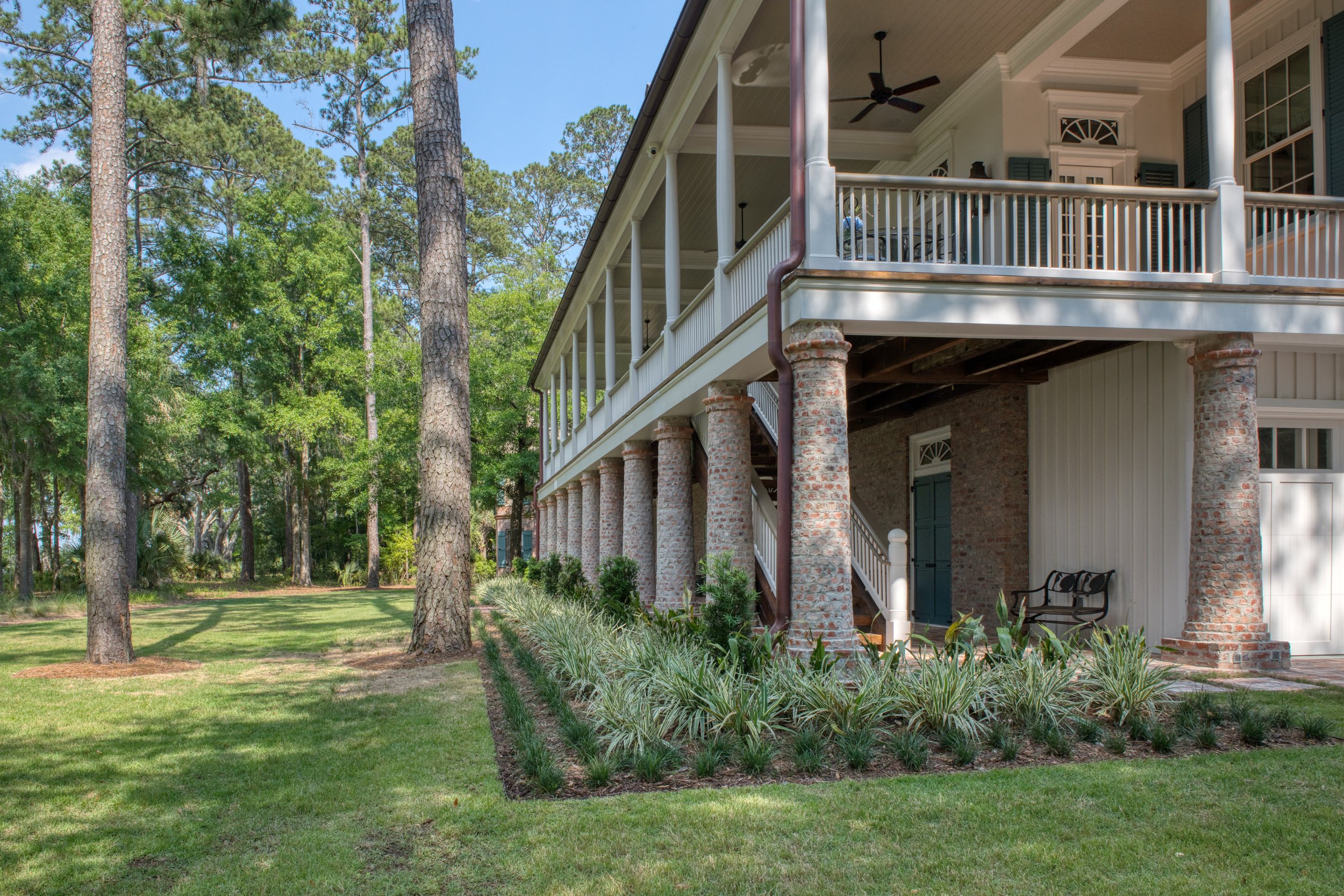 A house with a brick column porch, a landscaped yard, tall trees, and a clear sky.
