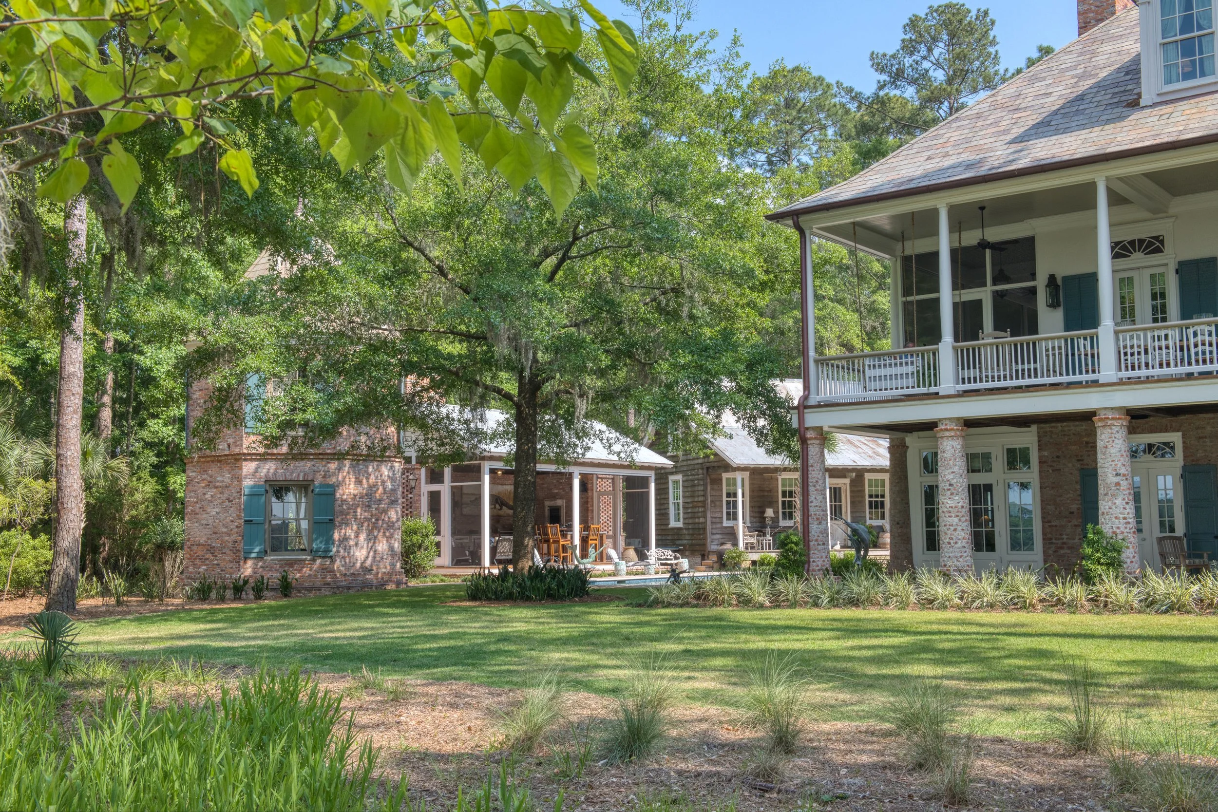 Large backyard view of a house with a screened porch, patio furniture, and a garden with grass and trees.