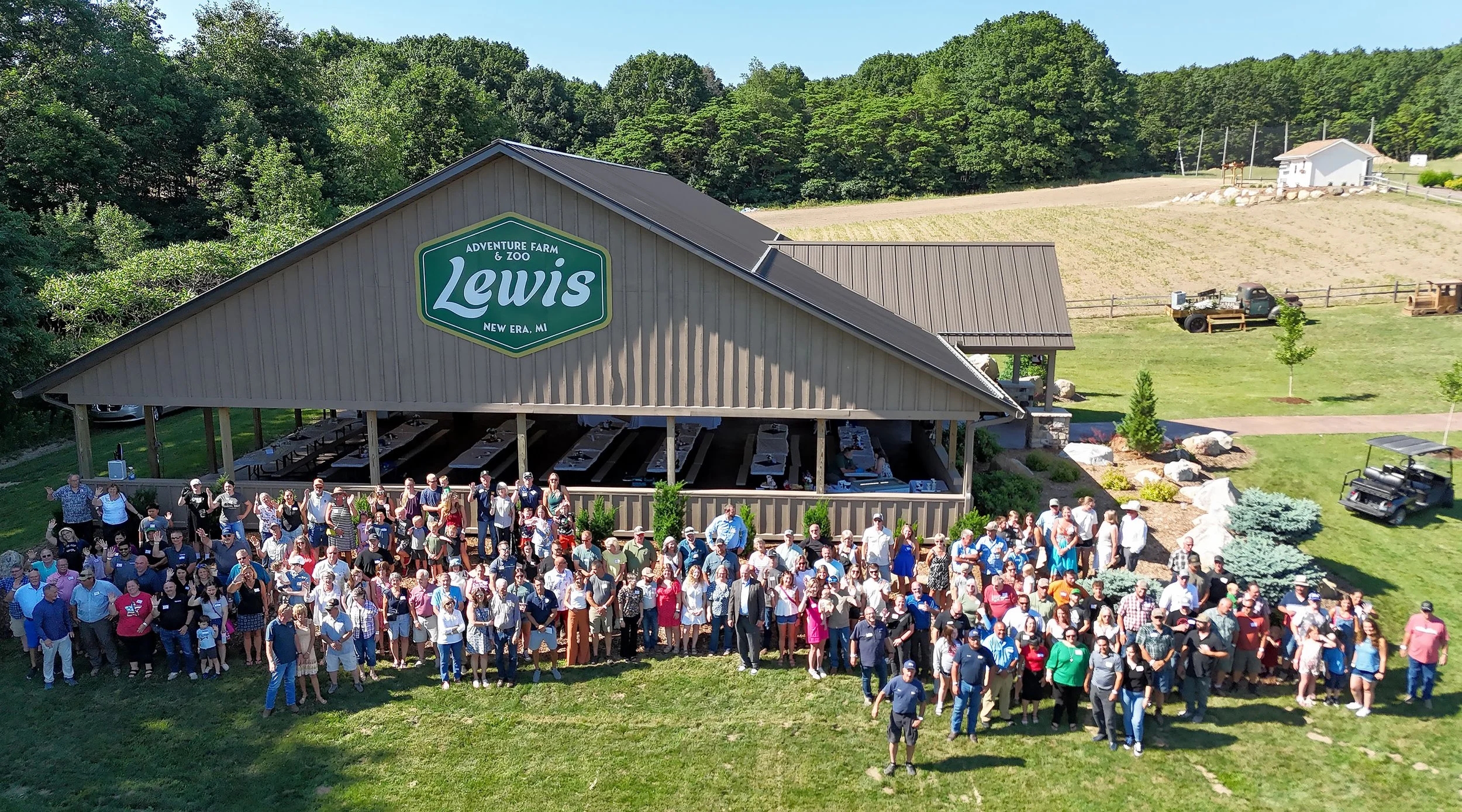 Two men talking asparagus farming in a field with trees in the background, one in a green hoodie and camouflage hat, the other in a brown jacket and blue shirt.