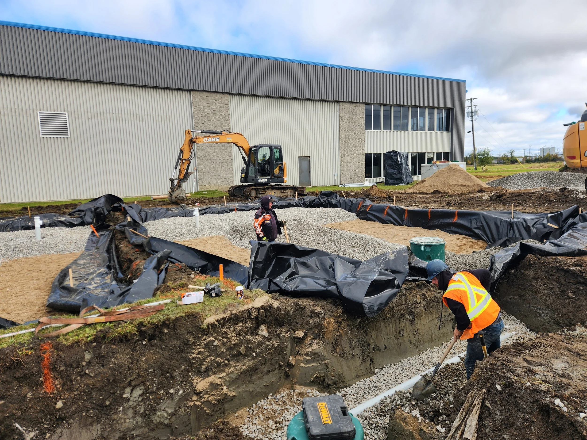 Chantier de construction avec ouvriers, pelleteuse, terre en excavation, et bâtiment en arrière-plan.