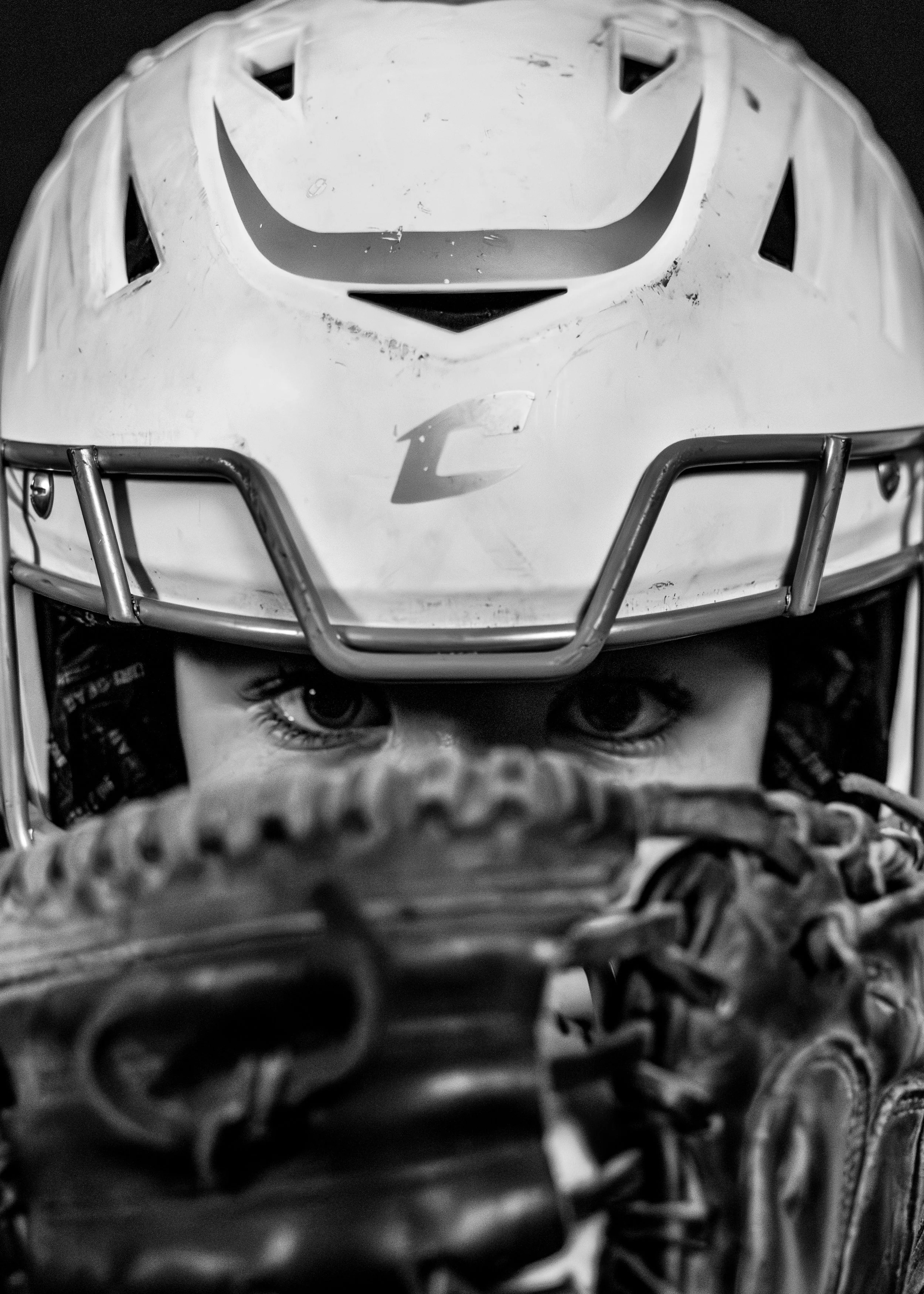 A young boy wearing a baseball cap and a baseball glove held up close to his face, with intense eyes gazing forward.