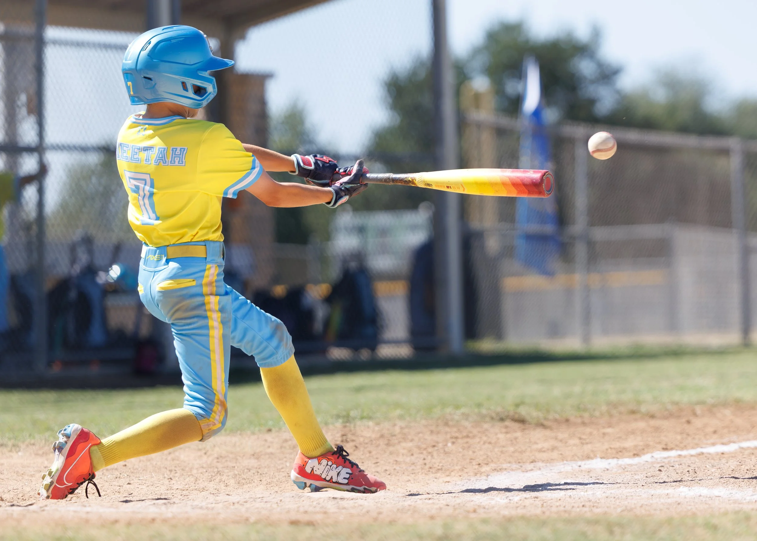 Young baseball player in uniform swinging a bat on the field, wearing a helmet and protective gear.