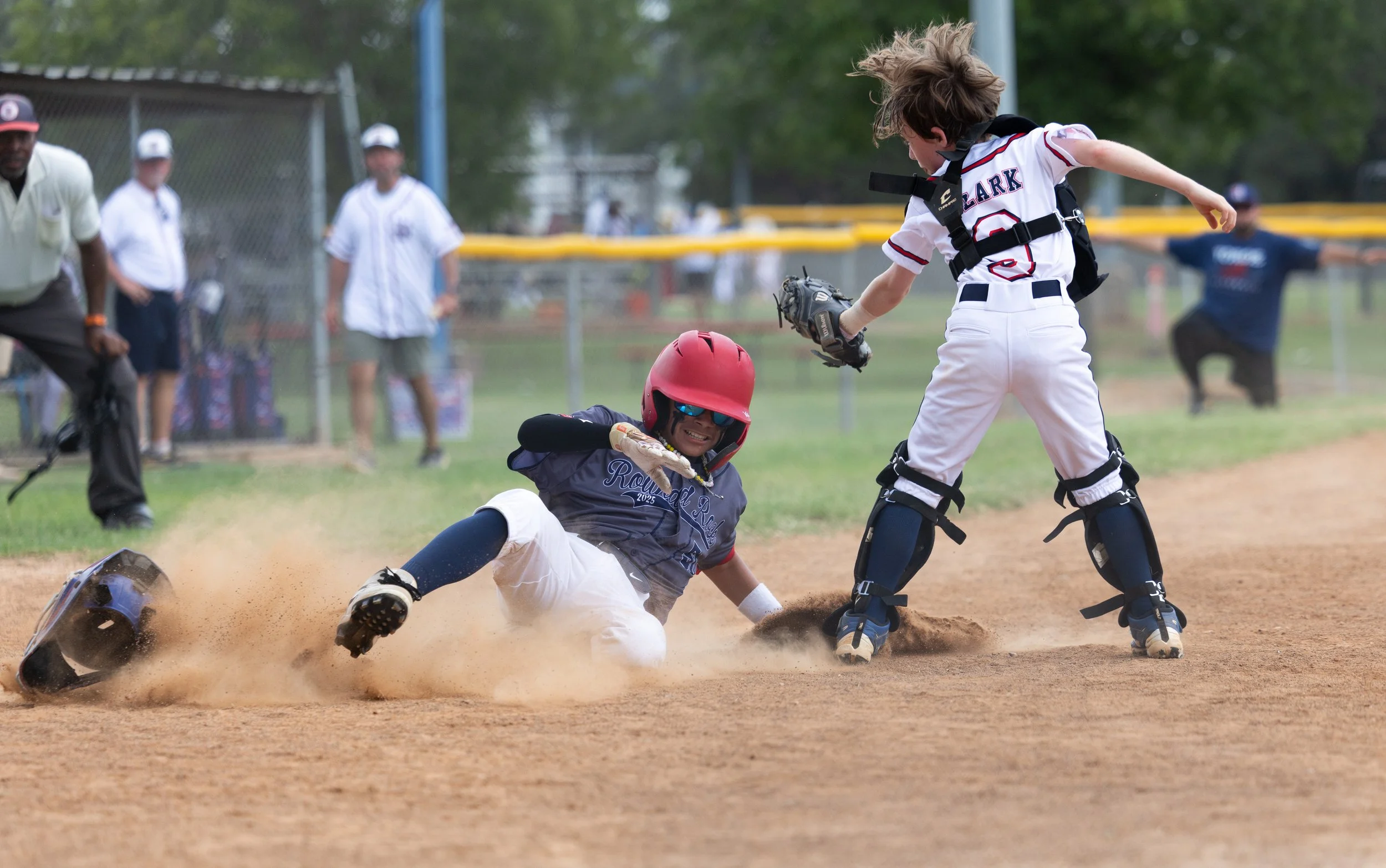 A young baseball player sliding into home plate while the catcher tries to tag him out during a game.