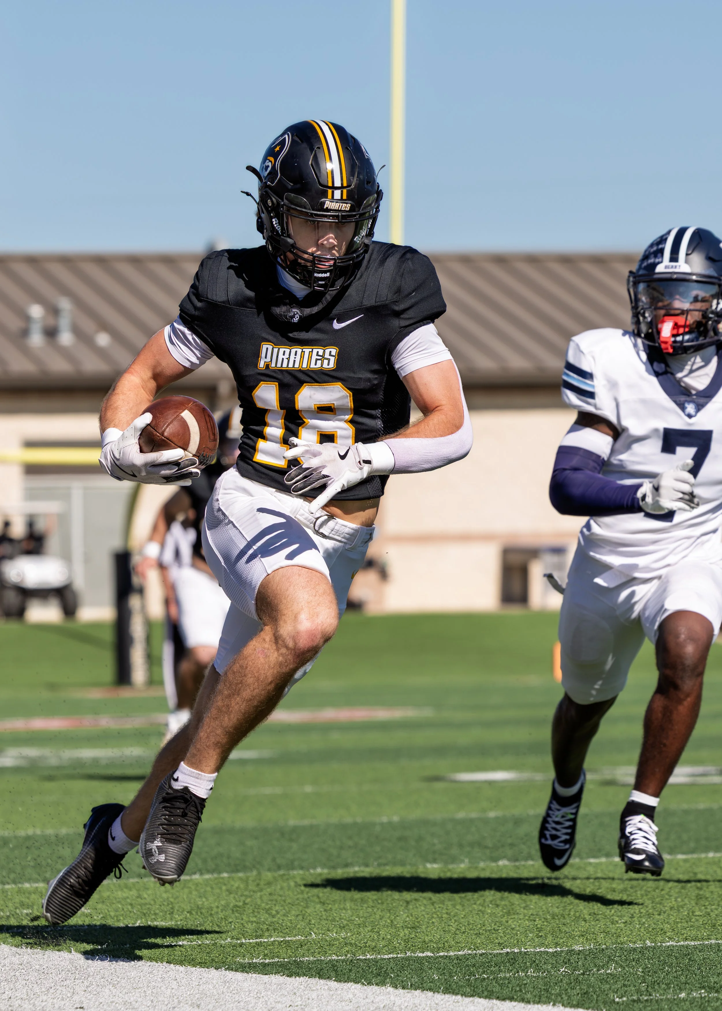 A football player in a black jersey with number 18 running with the ball during a game on a sunny day.