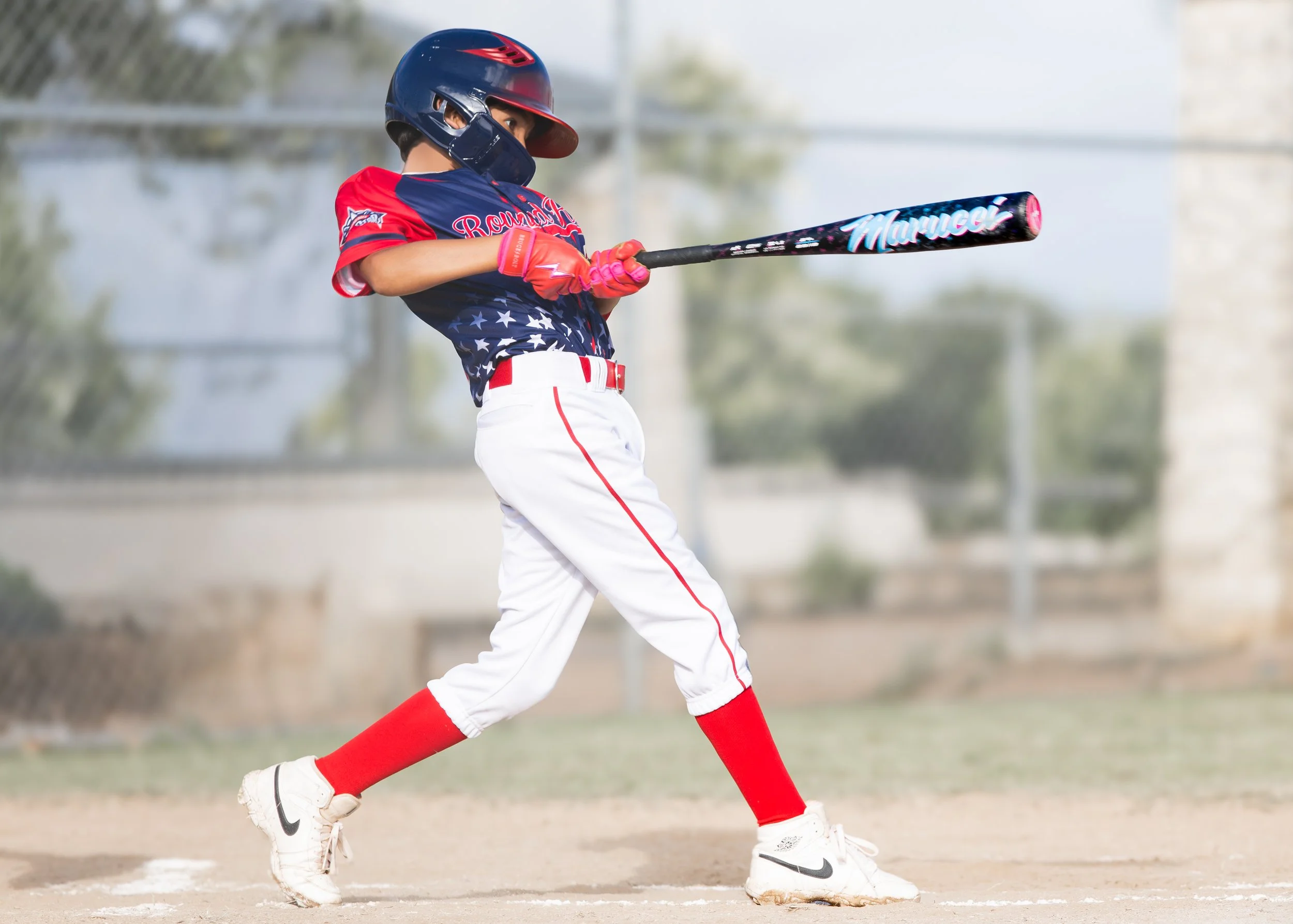 Young baseball player in uniform swinging a bat on the field, wearing a helmet and protective gear.