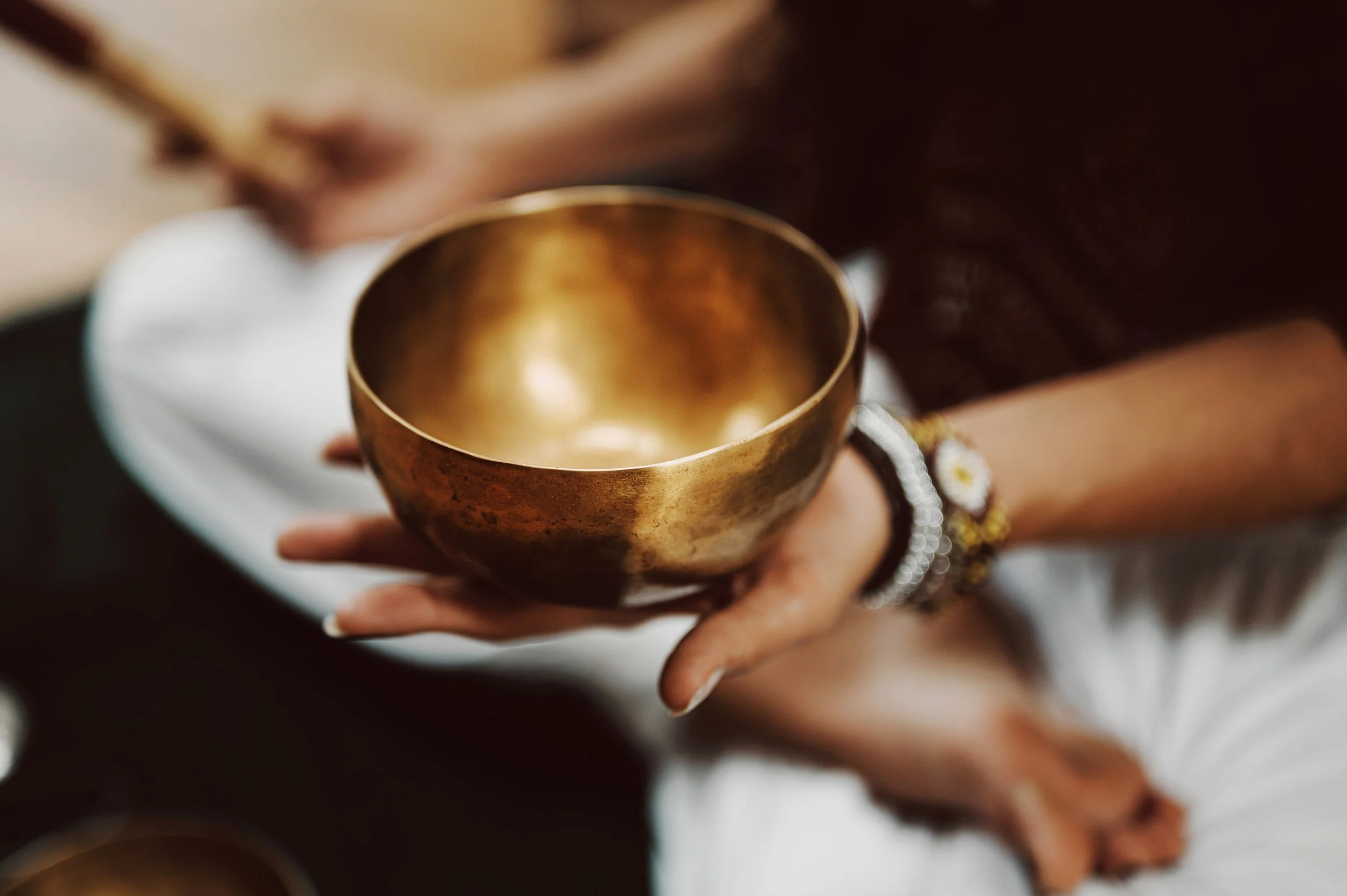 Person holding a brass singing bowl, wearing a white shirt and bracelets.