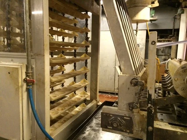 Industrial pastry equipment with racks of unbaked dough and machinery for baking and processing pastries.