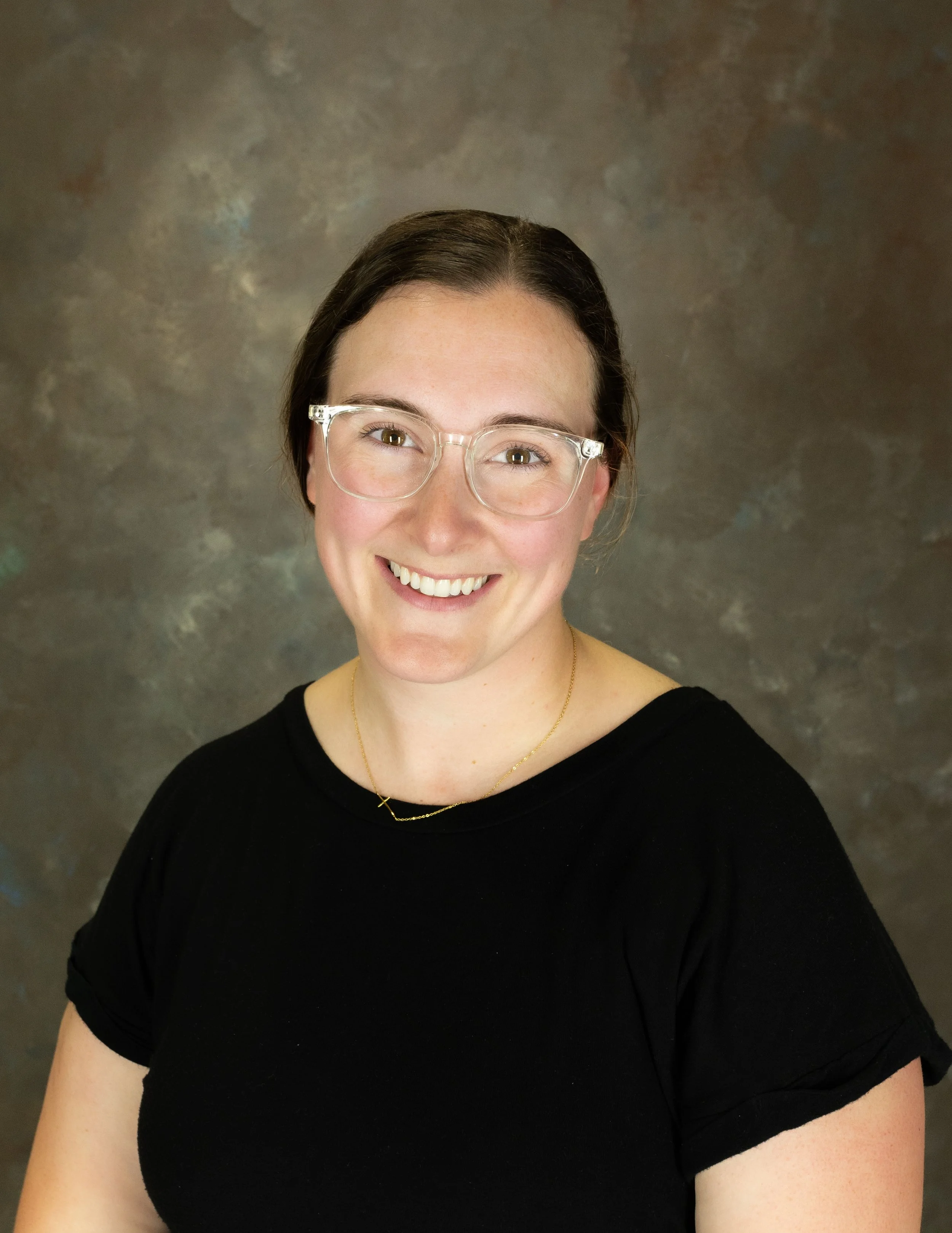 Smiling woman with glasses against a dark background.