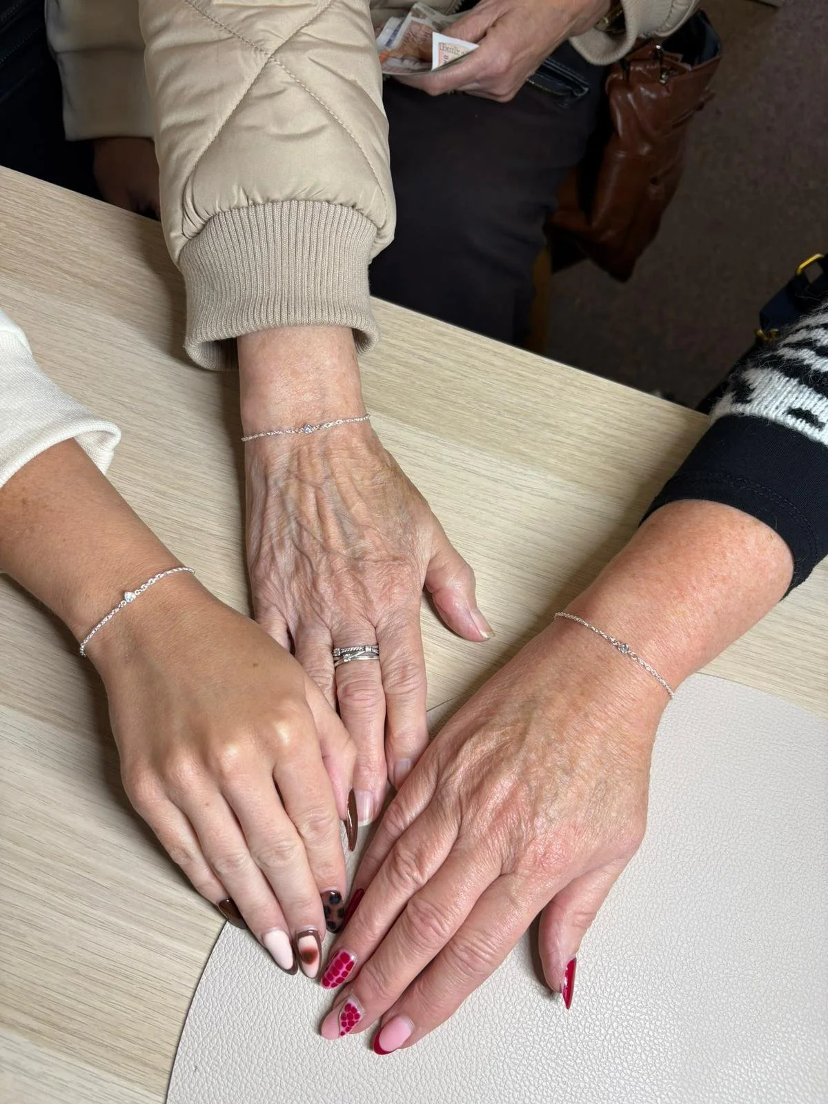 Three hands with jewelry resting on a table, showcasing rings and bracelets.