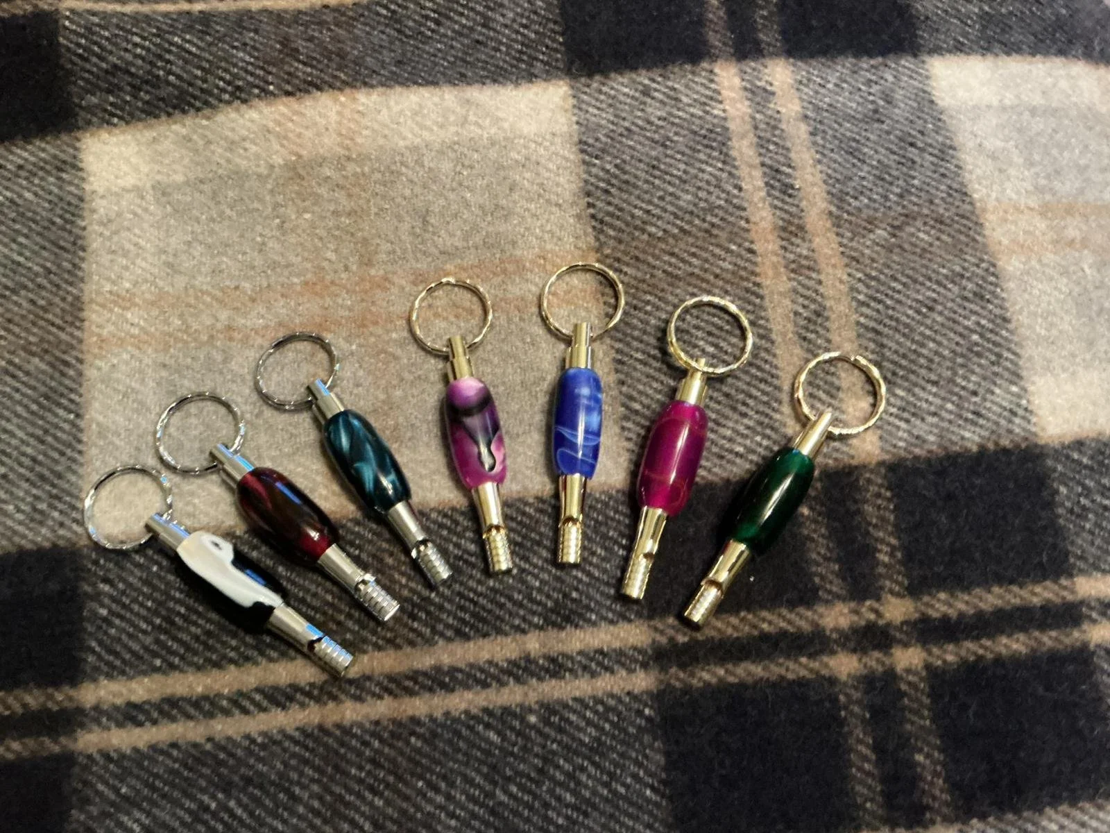 Six tobacco pipe miniature keychains with different colored bowls arranged in a row on a checkered cloth background.