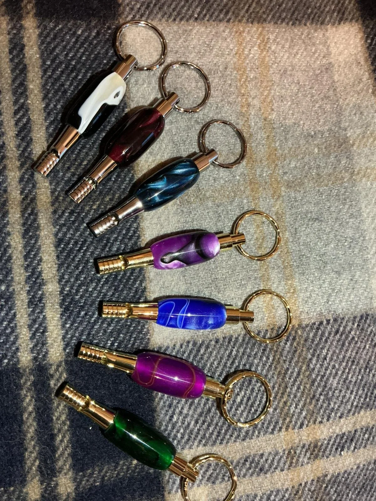 Six colorful glass and metal keychains arranged in a line on a textured surface.