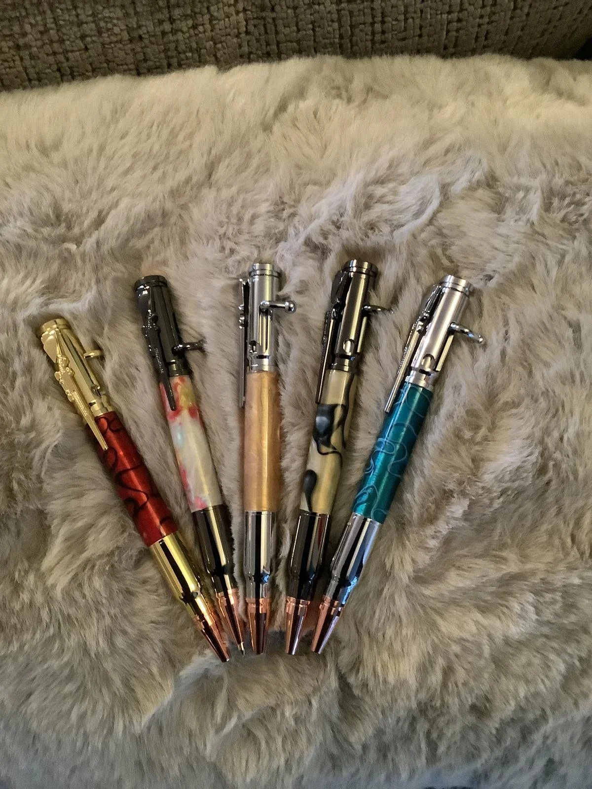 Five colorful pens with metallic tips, arranged in a row on a soft, furry surface.