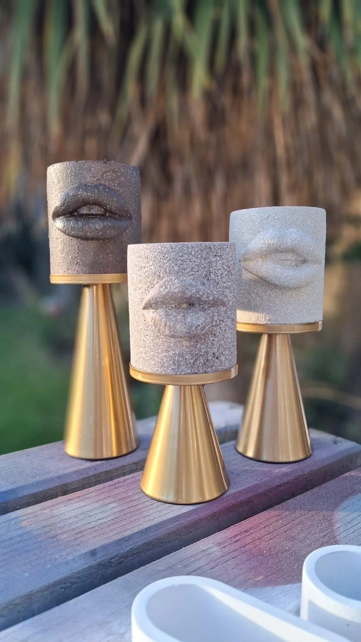 Three decorative sculptures of lips on cylindrical stone bases, placed on golden conical stands outdoors.
