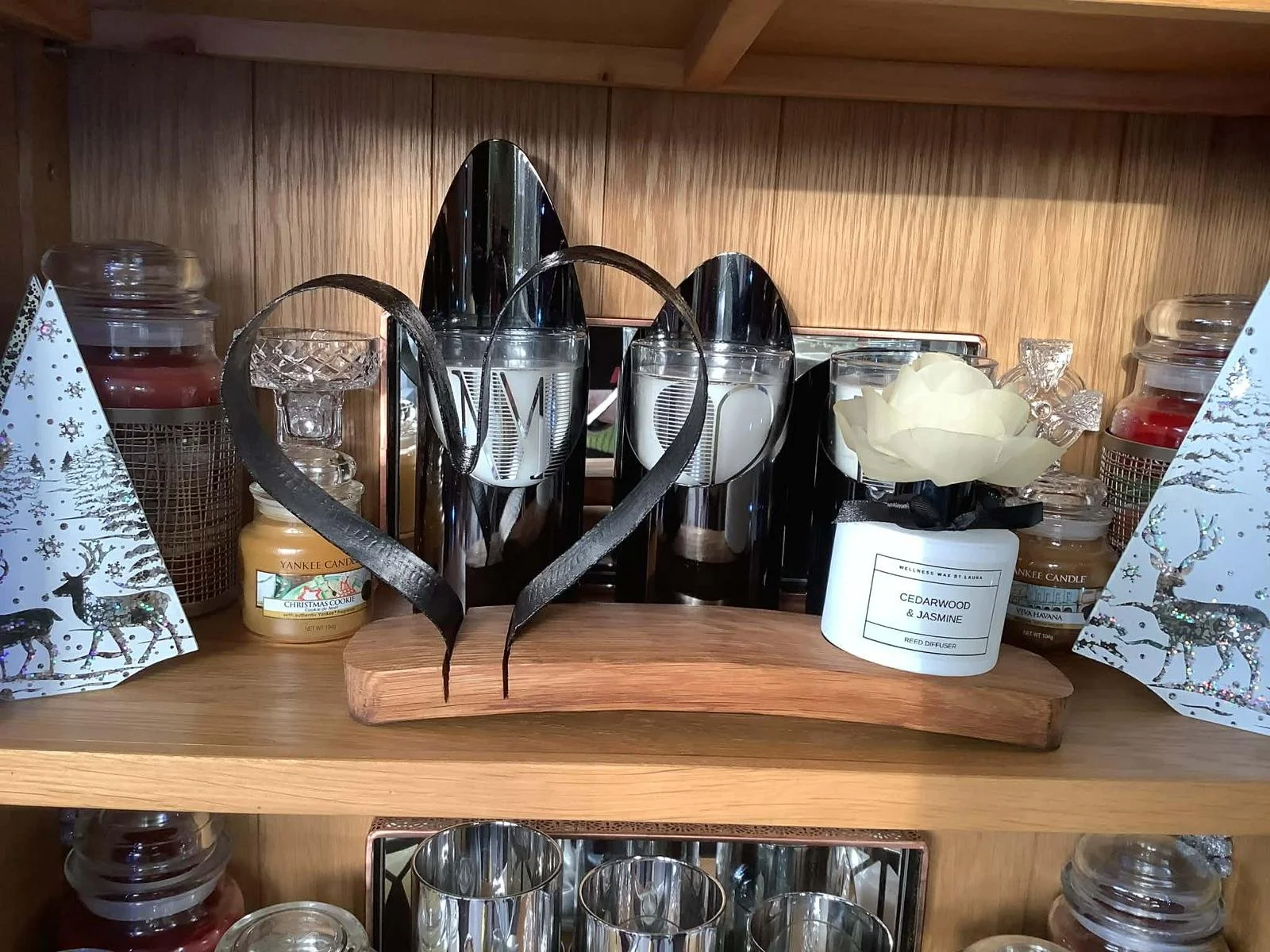 Decorative wooden shelf with holiday candles, glassware, a white diffuser labeled cedarwood and jasmine, and holiday-themed boxes with reindeer and snowflakes.