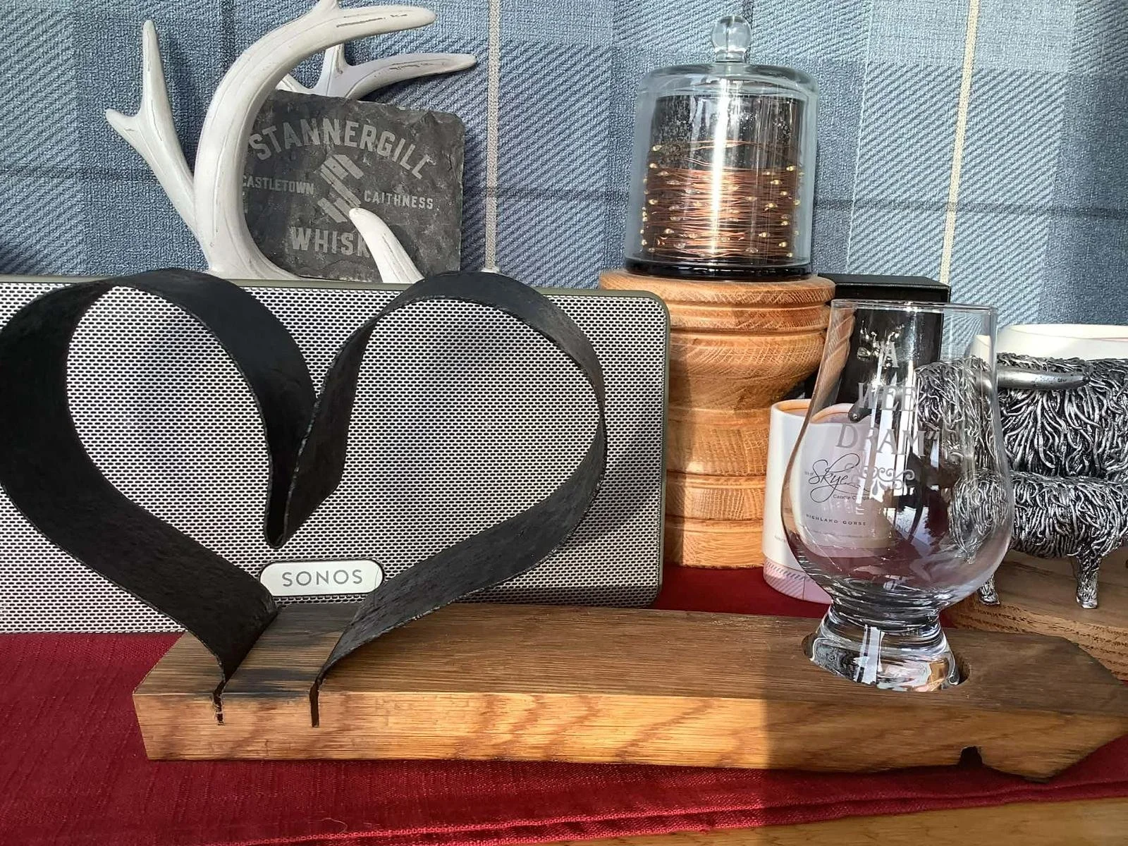 Decorative display featuring a metal heart sign with the brand name 'Sonos', a white antler decoration, a glass container with copper coils on a wooden base, a glass with the words 'Dream' and 'Sky' on it, and a silver ornate miniature chair on a woo