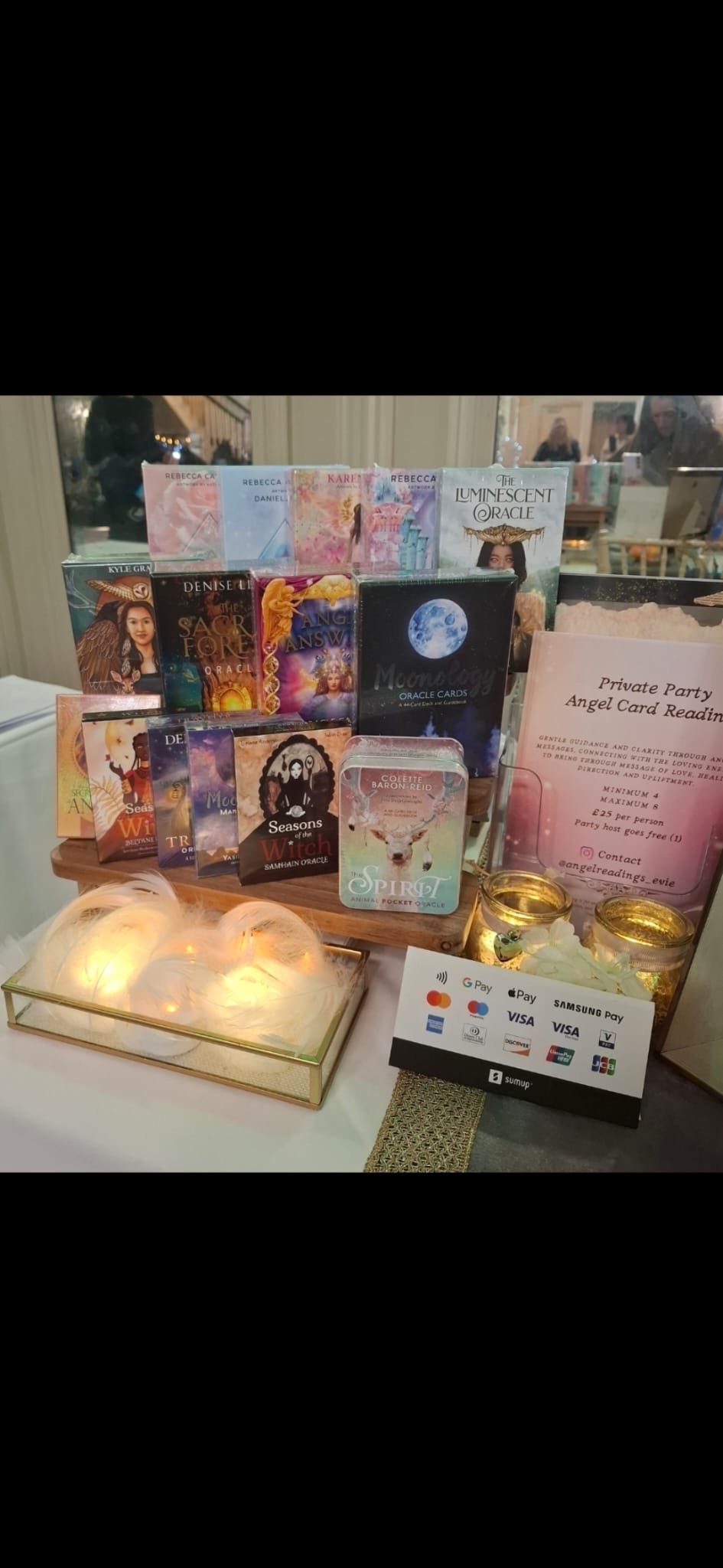 Display of tarot cards, oracle cards, and angel reading cards at a private party, with a sign detailing the event and contact information, and a box with glowing lights.