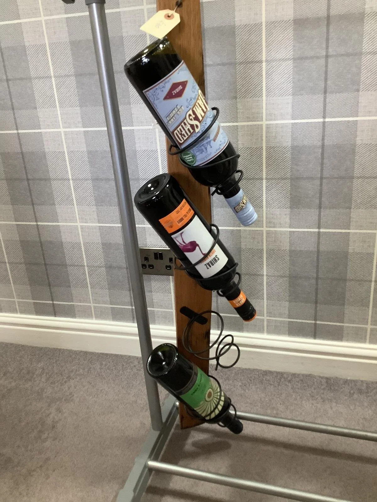 Vertical wine bottle holder attached to a wooden board, holding four bottles of wine with labels facing outward.