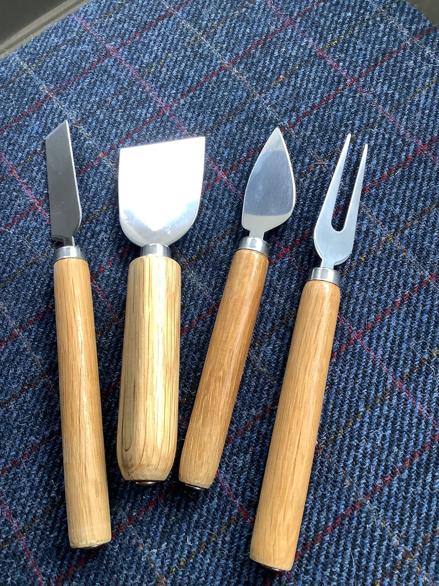 Set of four cheese knives with wooden handles on a checkered fabric surface.