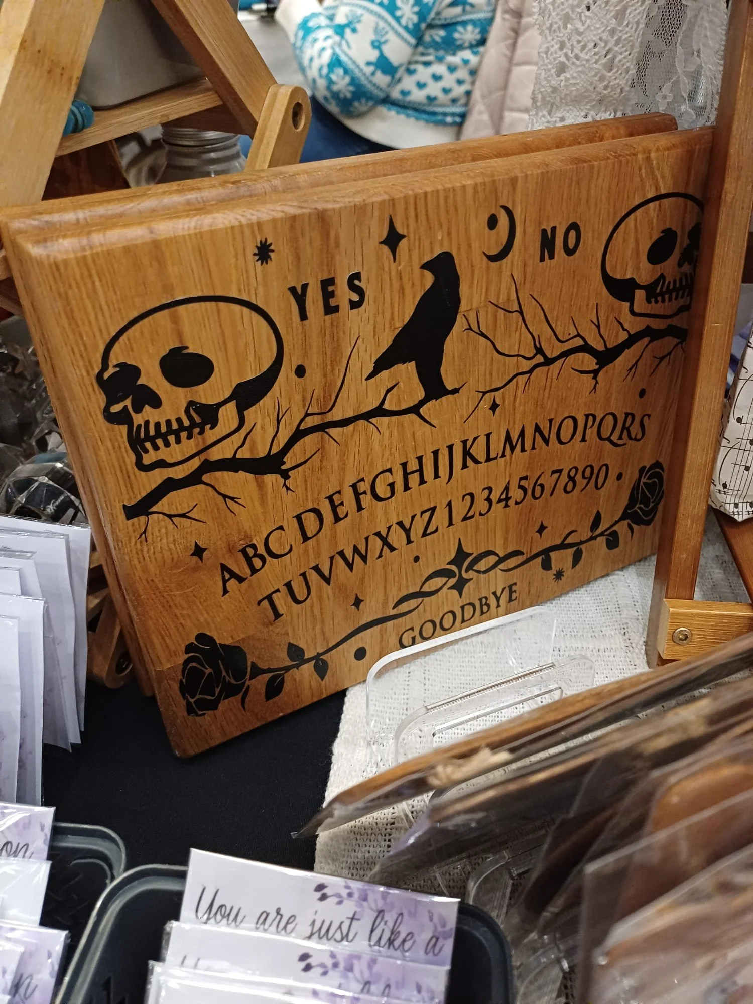 A wooden Ouija board with black symbols, including skulls, a raven, and alphabet letters, with 'YES', 'NO', and 'GOODBYE' printed on it.