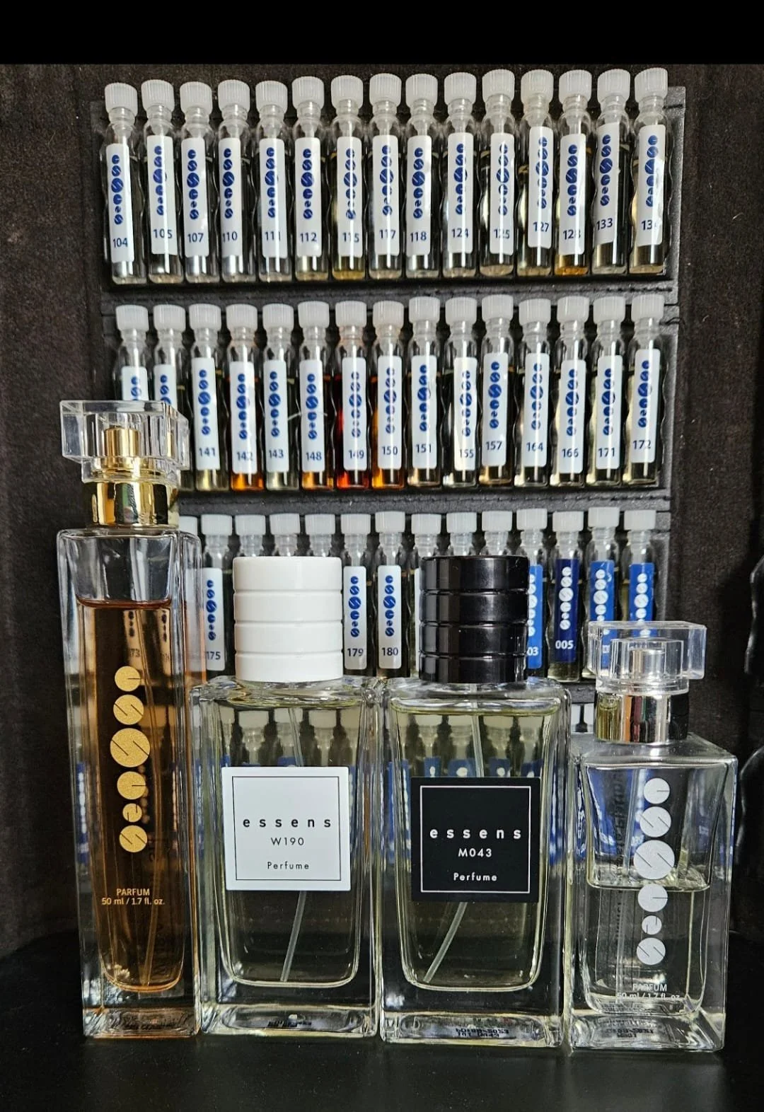 Display of perfume bottles and sample vials of perfume scents in a store or setup, with the bottles labeled 'essens' and various bottle shapes and sizes.