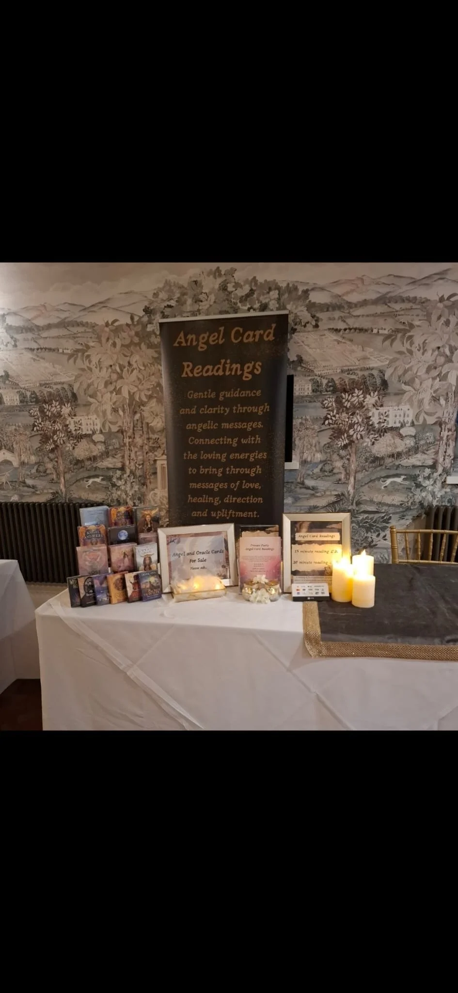 Display table with angel card readings at an event, featuring tarot and oracle cards, candles, and informational signs.