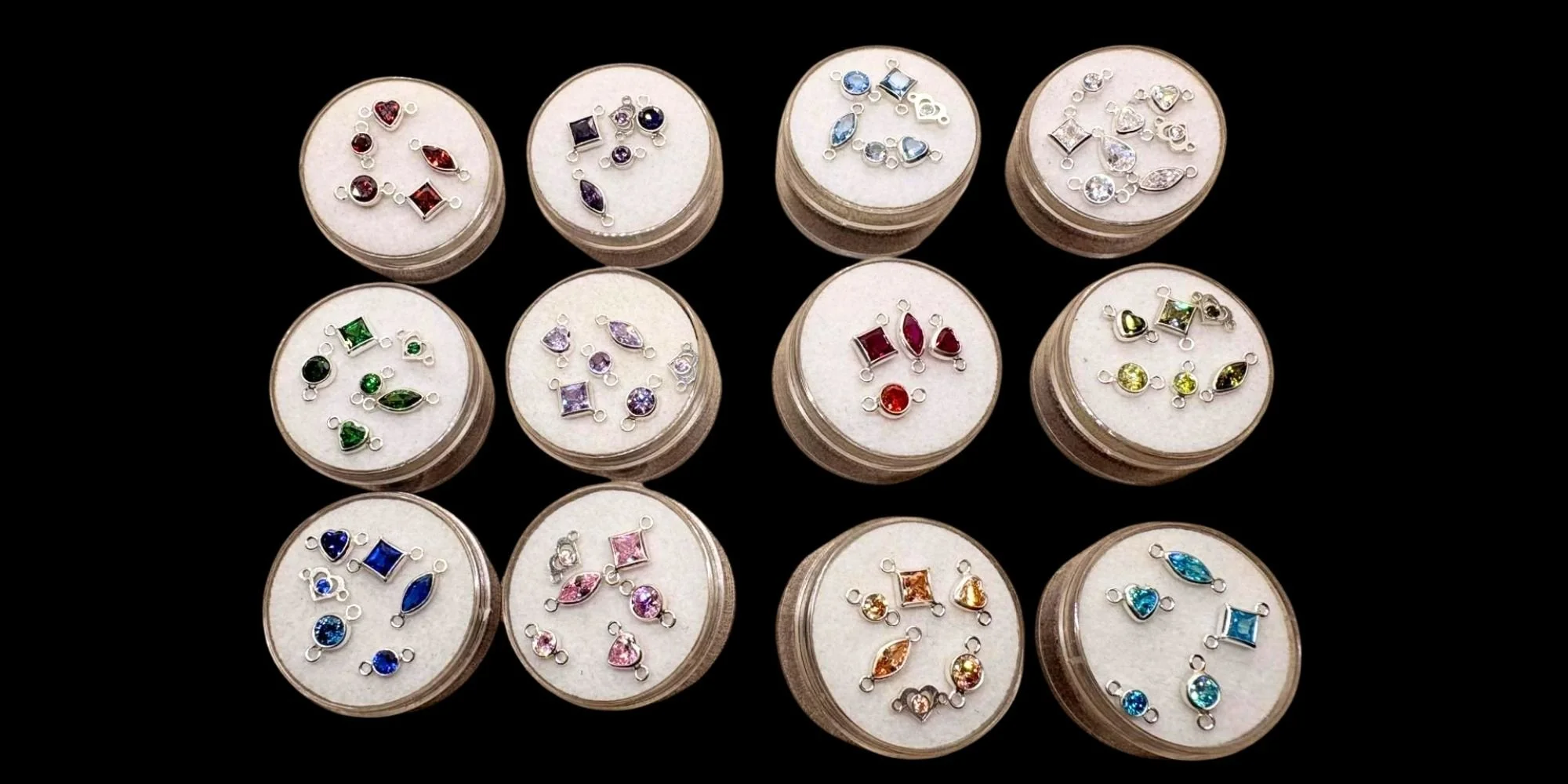 Display of various colorful gemstone pendants arranged in circular containers on a black surface.