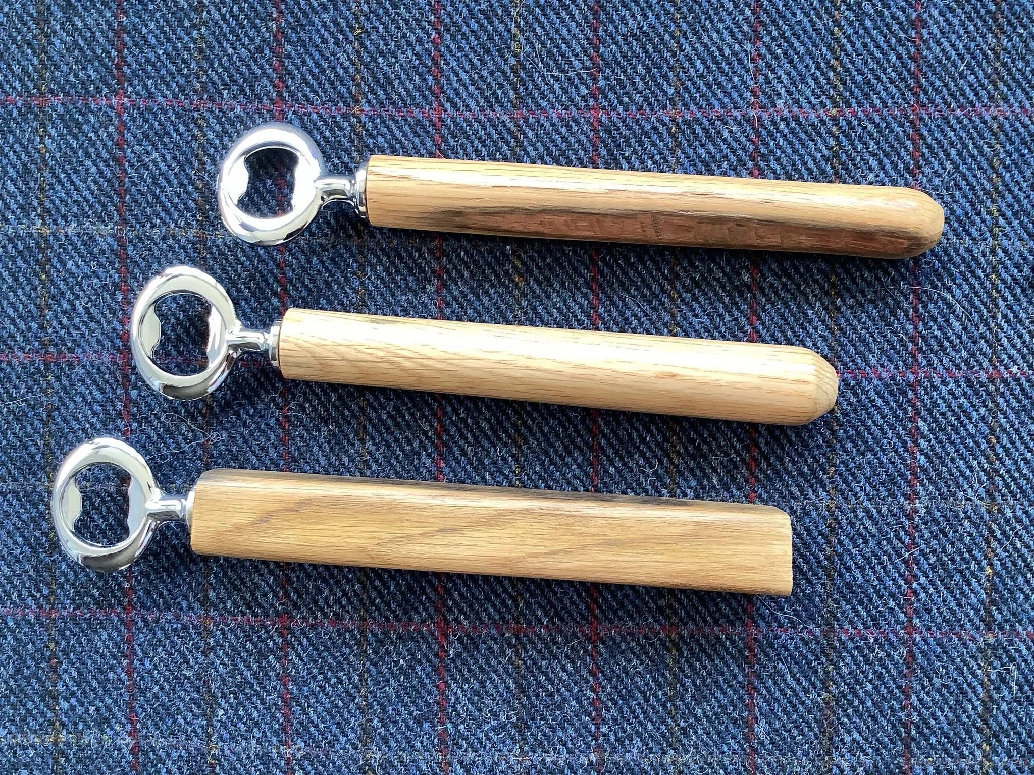 Three corkscrew bottle openers with wooden handles on a blue checkered fabric background.
