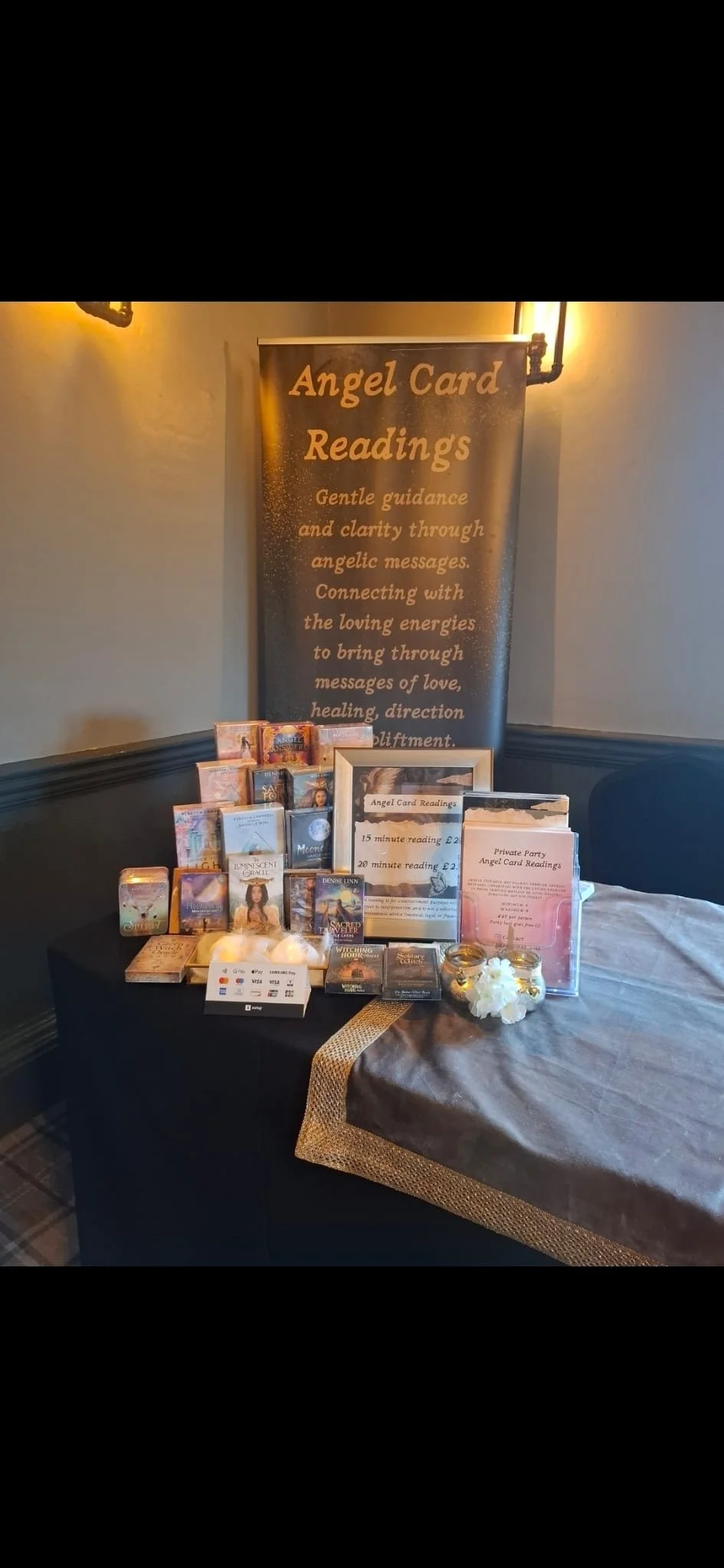 Table with angel card reading products, including cards, informational signs, and decorative items, set against a large banner advertising angel card readings.