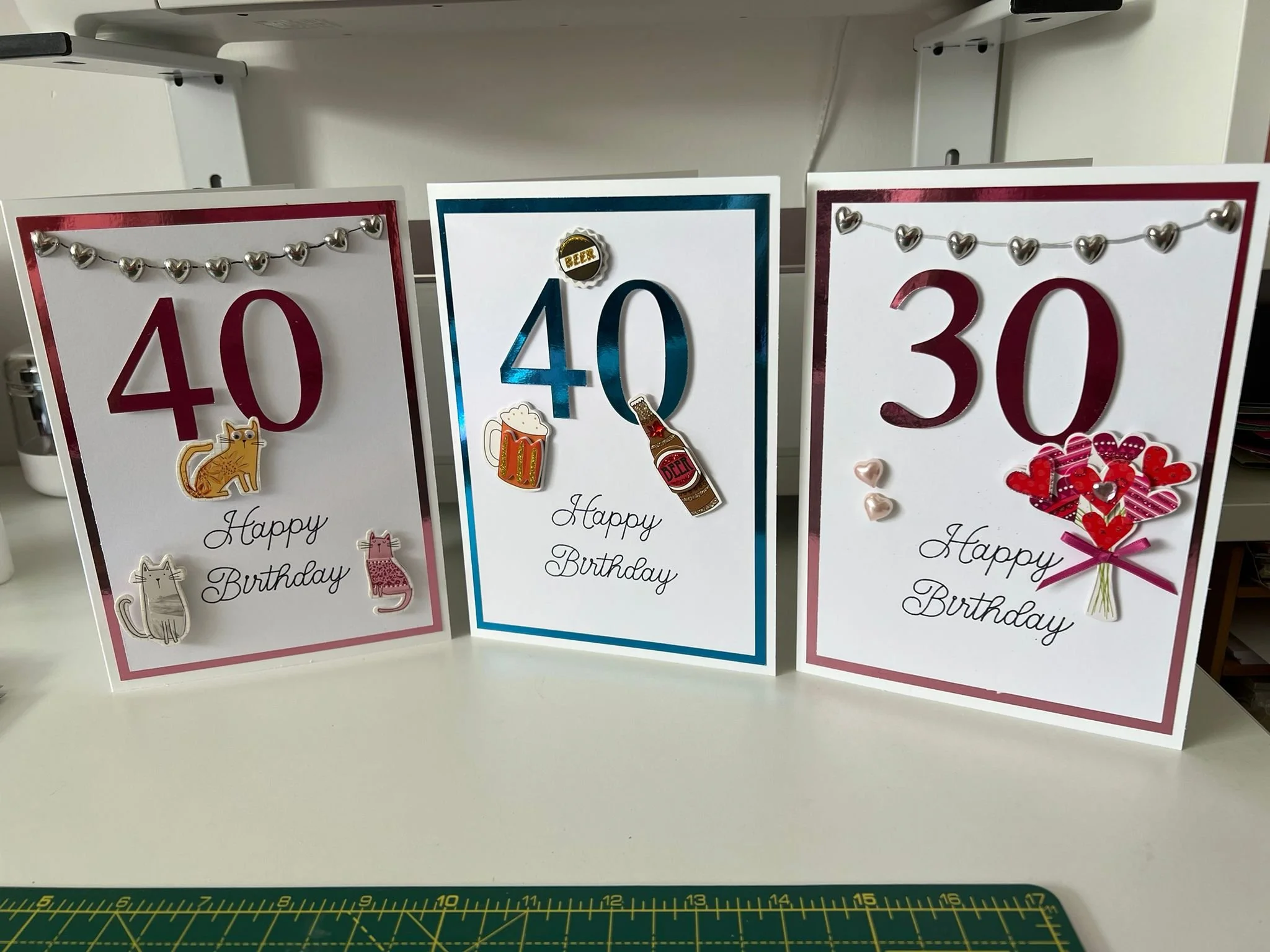 Three birthday cards with numbers 40, 40, and 30 celebrating age, decorated with stickers of animals, beverages, and hearts, with the message "Happy Birthday" written on each.