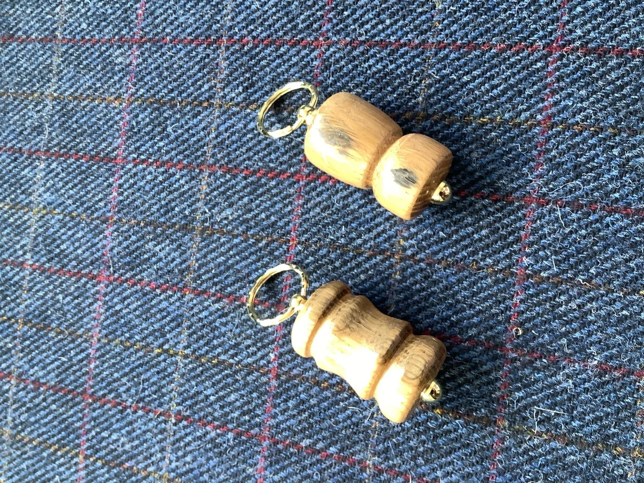 Wooden keychain with two wooden blocks connected by a metal ring, placed on a blue and red plaid fabric background.