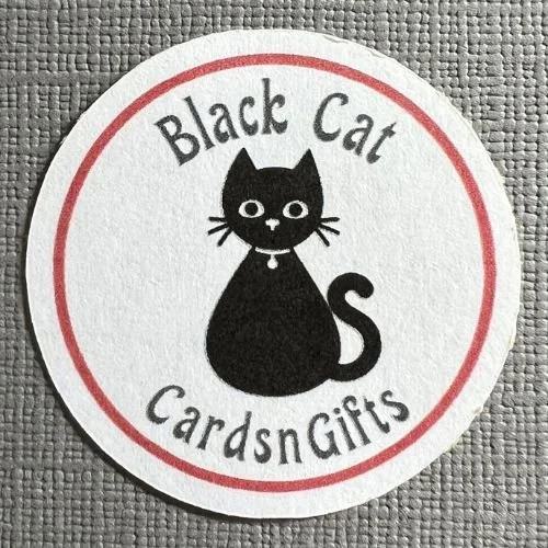 Round logo with a black cartoon cat in the center, the cat has white eyes and a collar. Text around the cat reads "Black Cat Cards and Gifts."