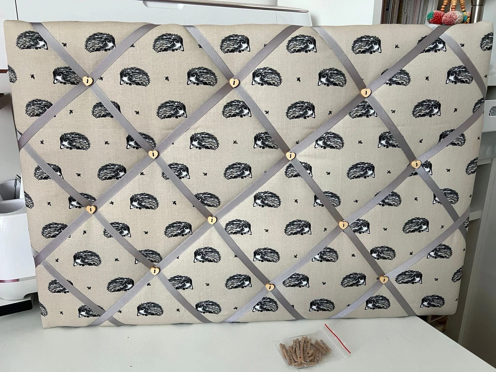 A beige upholstered headboard with a pattern of black and white hedgehogs, secured with gray straps and wooden buttons arranged in a diamond shape.
