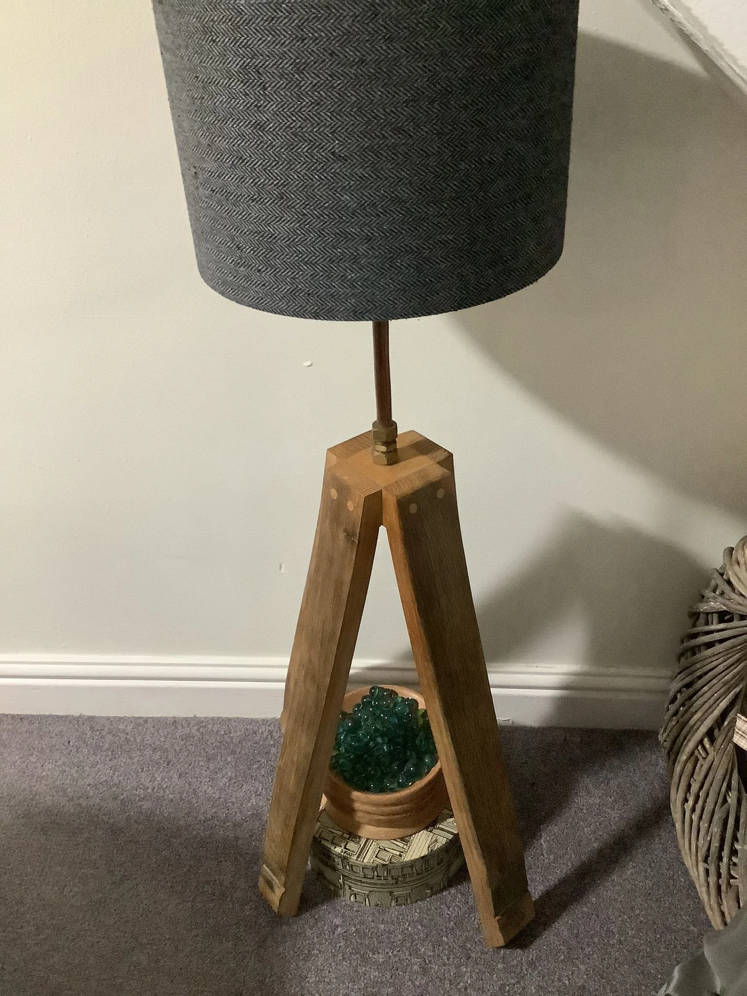 A tripod-style lamp with a fabric shade, wood legs, and a decorative bowl containing green glass stones underneath.