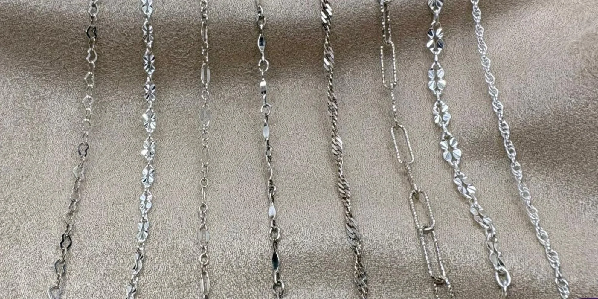 Several silver necklaces with various chain designs hanging on a display.