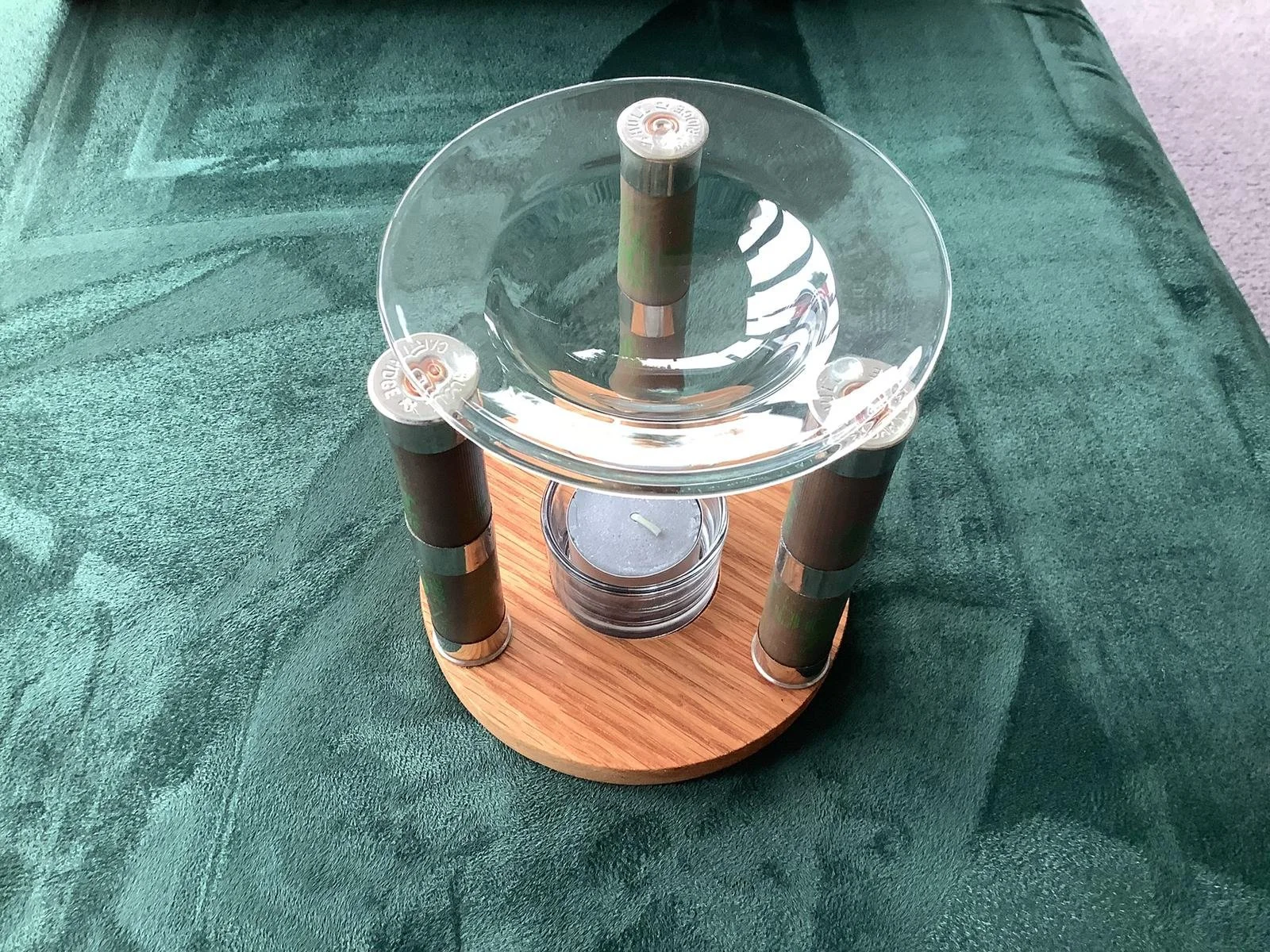 Decorative candle holder with four cylindrical green candles around a glass dish on a wooden base.